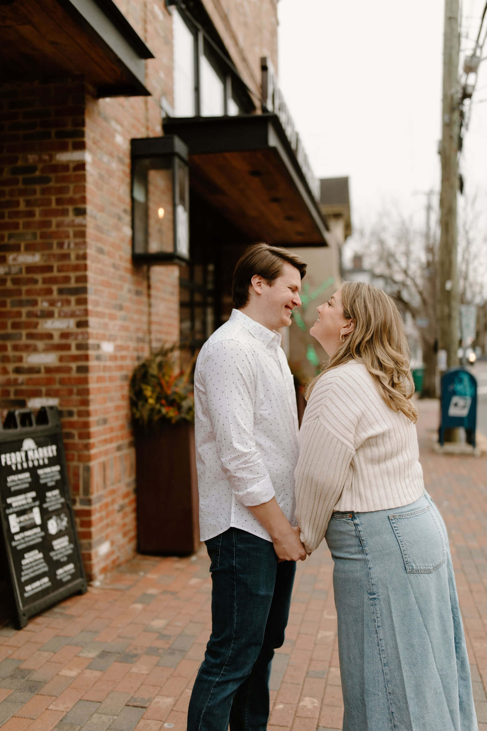 a man and a woman holding hands and laughing toward each other outside on a brick sidewalk