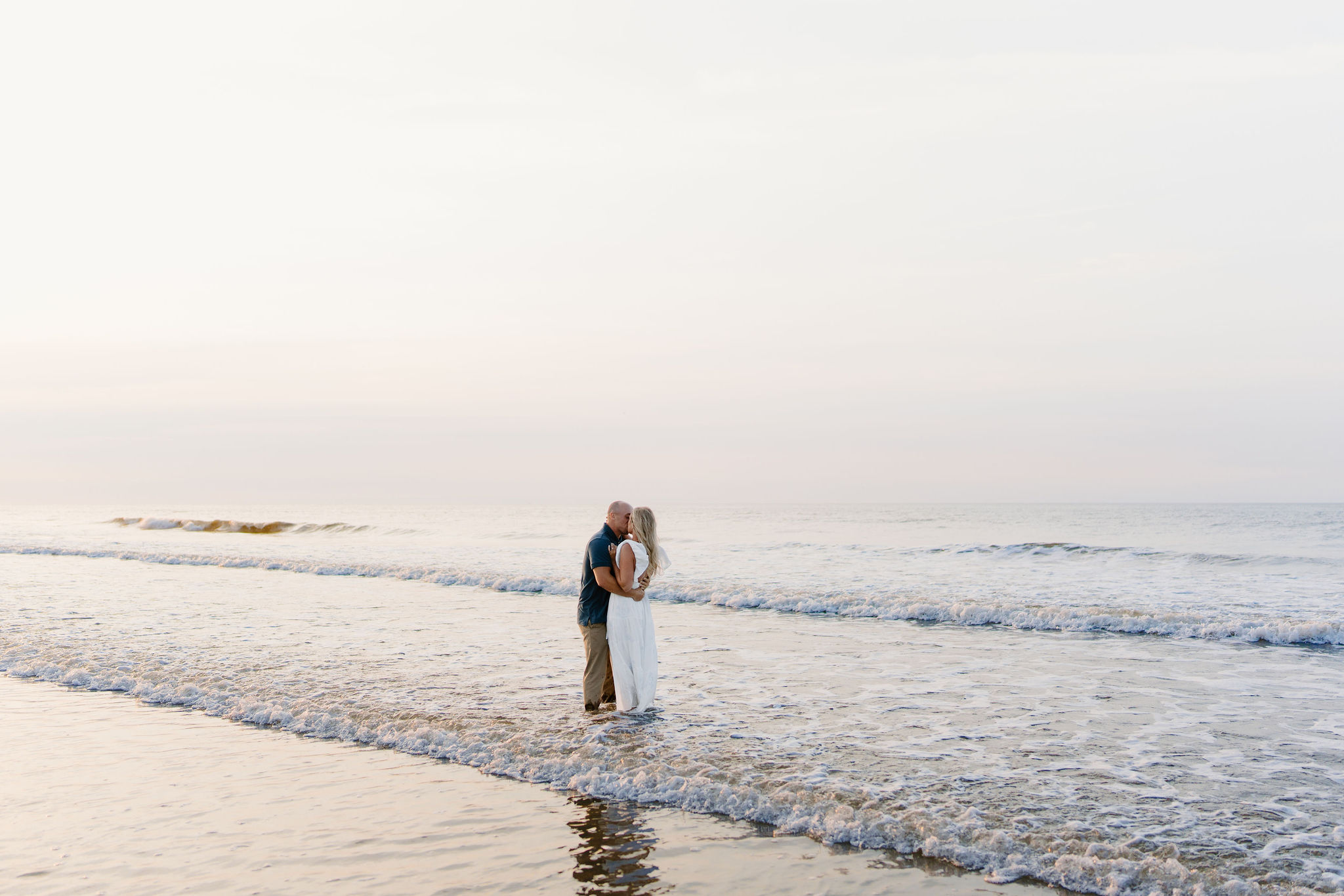 a couple taking their engagement pictures, embracing while standing in the waves