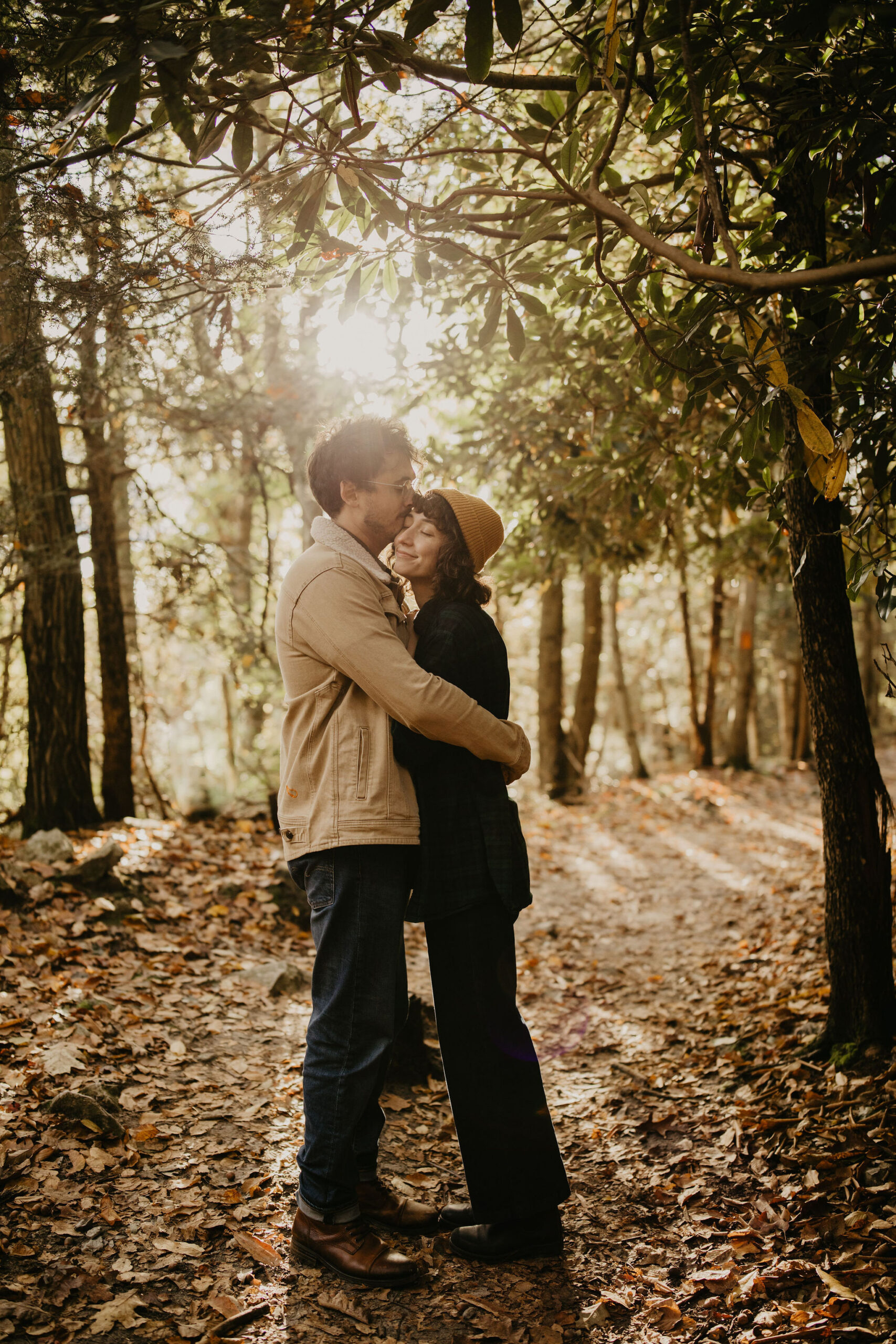 a man and a woman on a hiking trail, embracing while he kisses her forehead