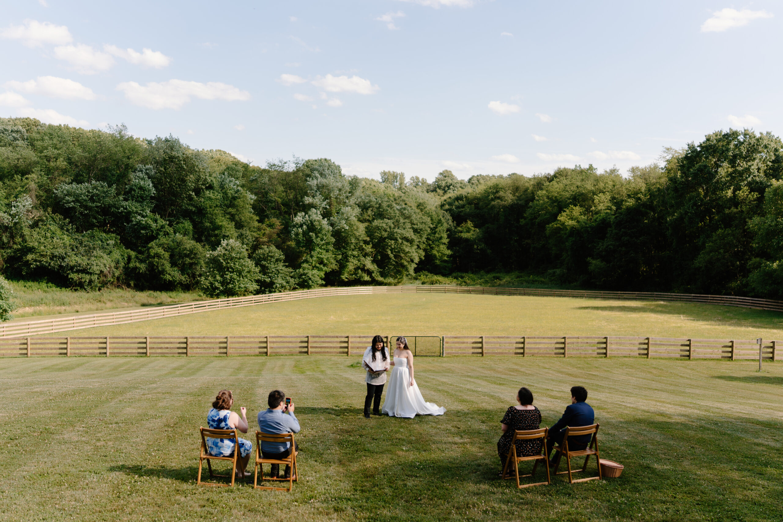 bride and groom exchanging vows in a meadow, with four of their closest friends sitting and watching