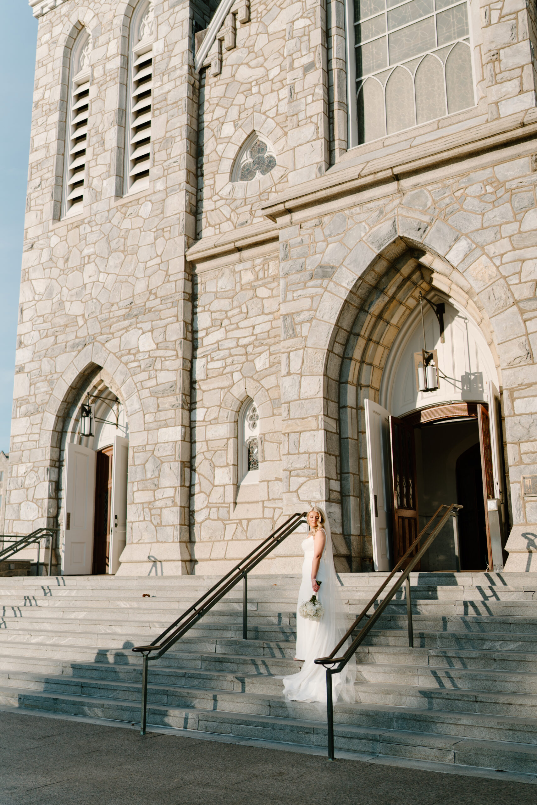 bride standing on steps to Villanova cathedral, looking over her shoulder and holding her bouquet down at her side