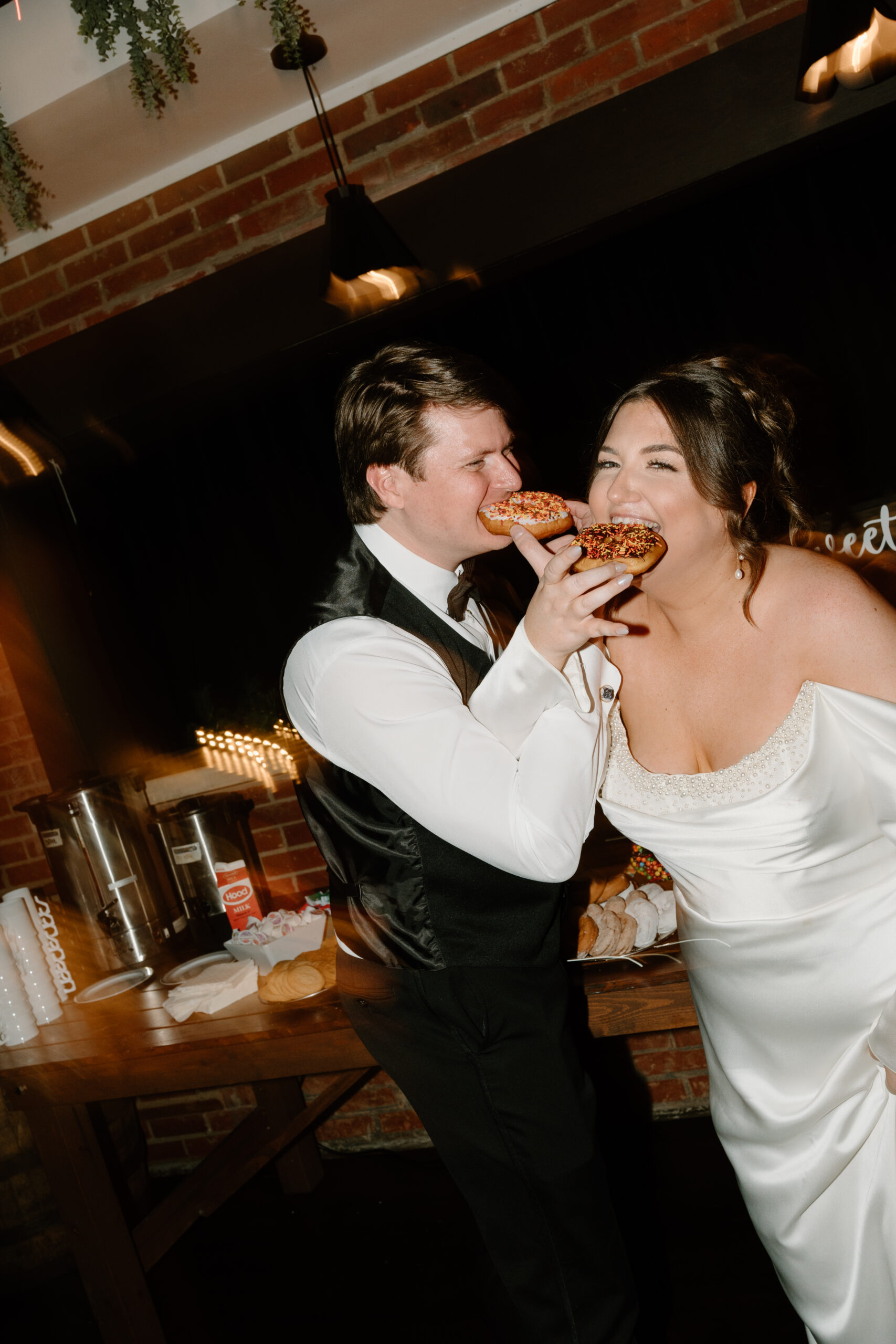 a bride and groom locking arms and taking a bite out of donuts and smiling at each other