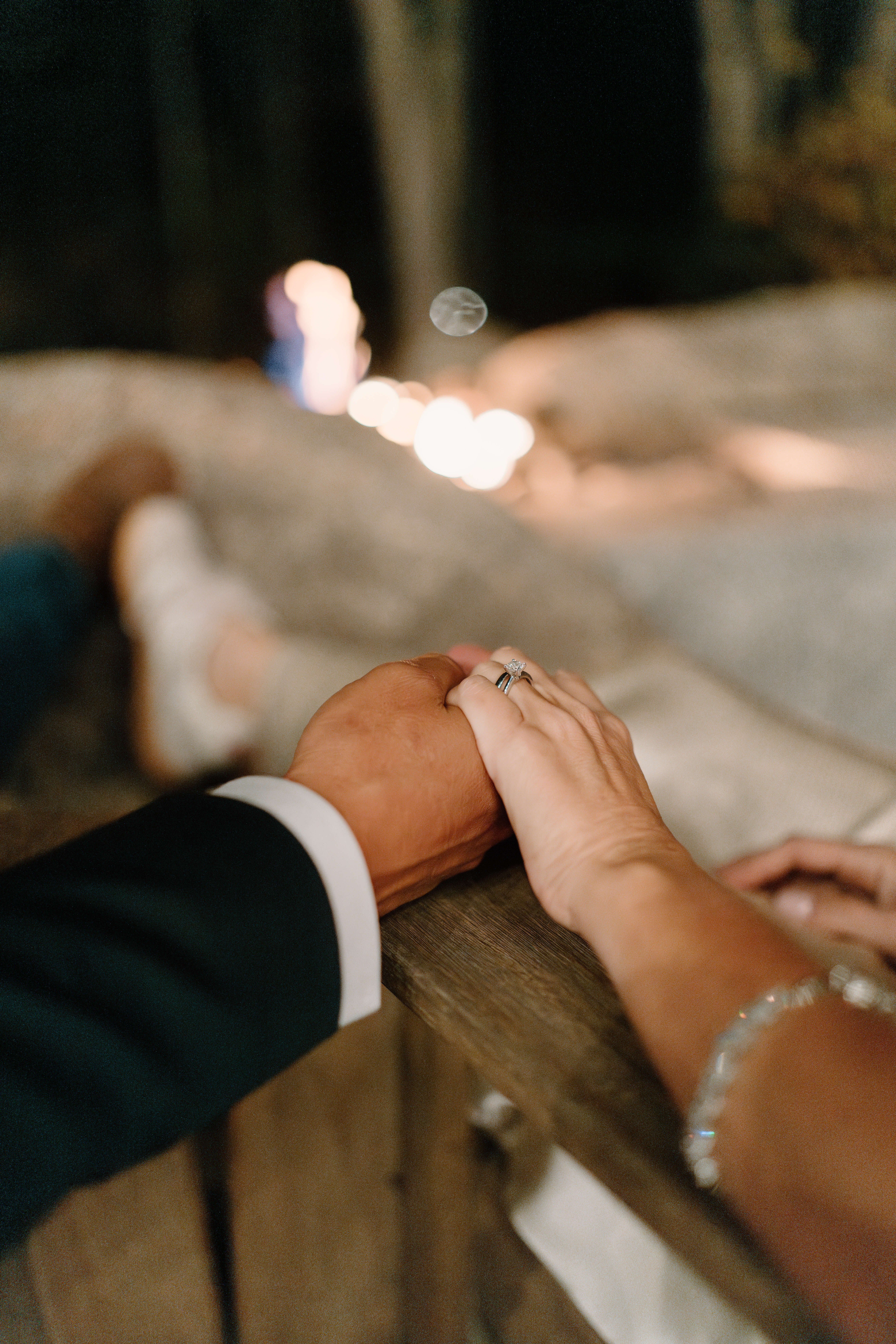 close up image of a bride and groom holding hands, with a fire roaring in the background, the focus on her engagement and wedding rings