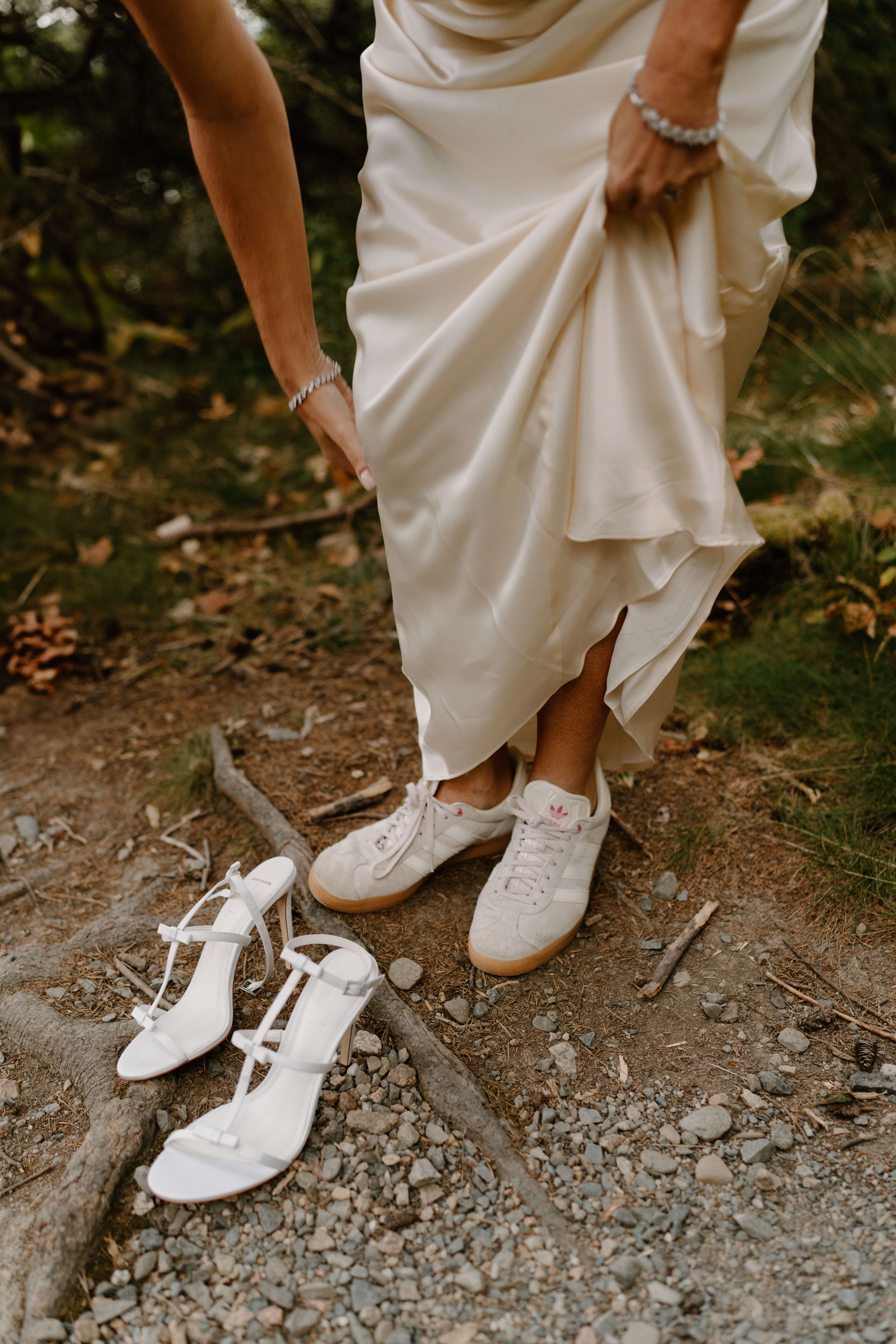 close up image of a bride bending down and lifting her skirt to change from her white sneakers into her white stiletto heels