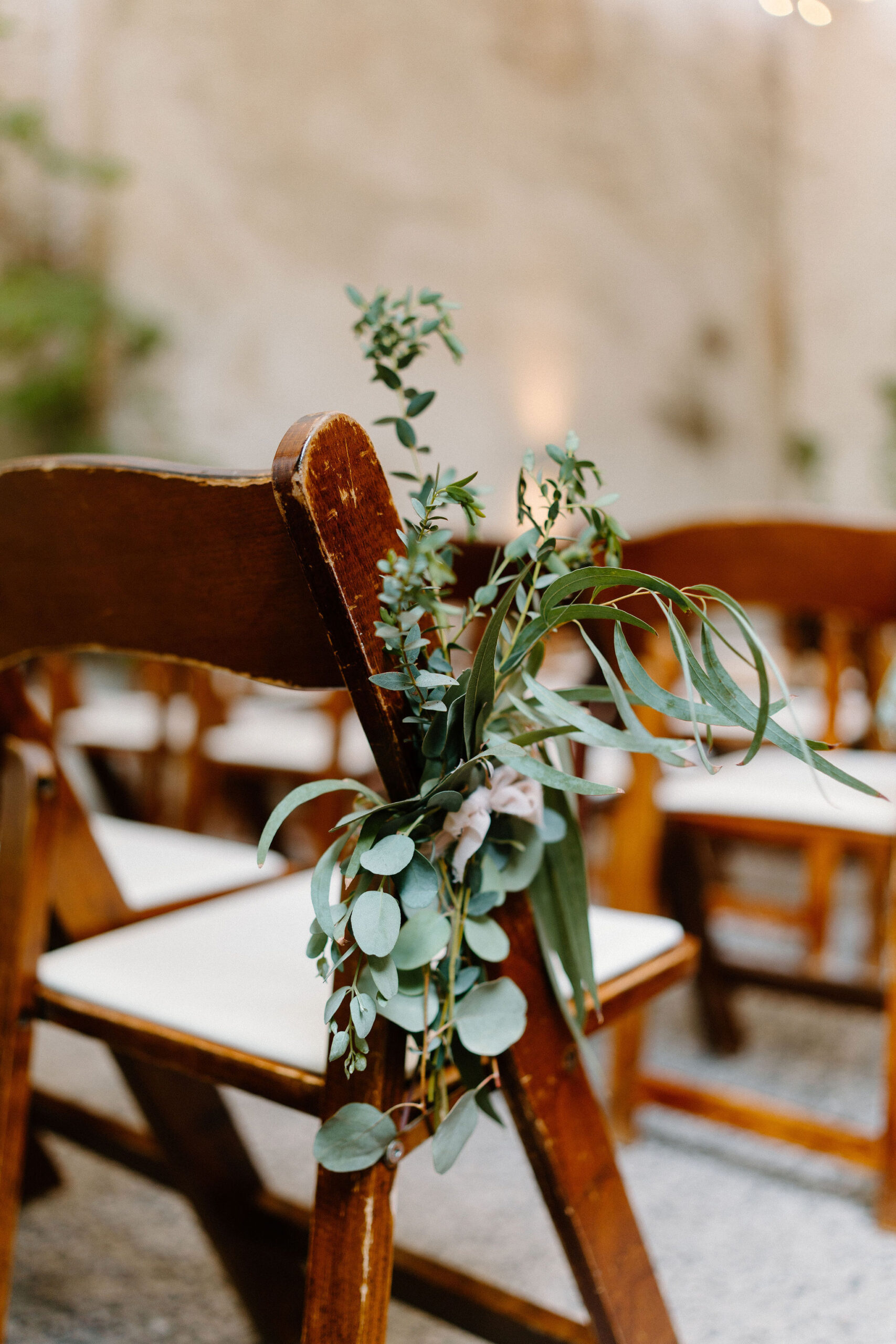 close up of a wooden ceremony chair, with a small bouquet of eucalyptus tied to the side