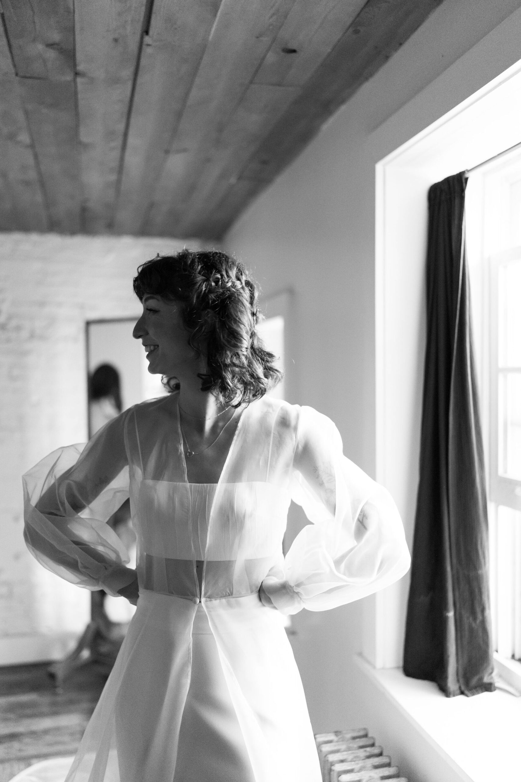 black and white image of a bride with her hands on her hips, smiling off camera toward her friends