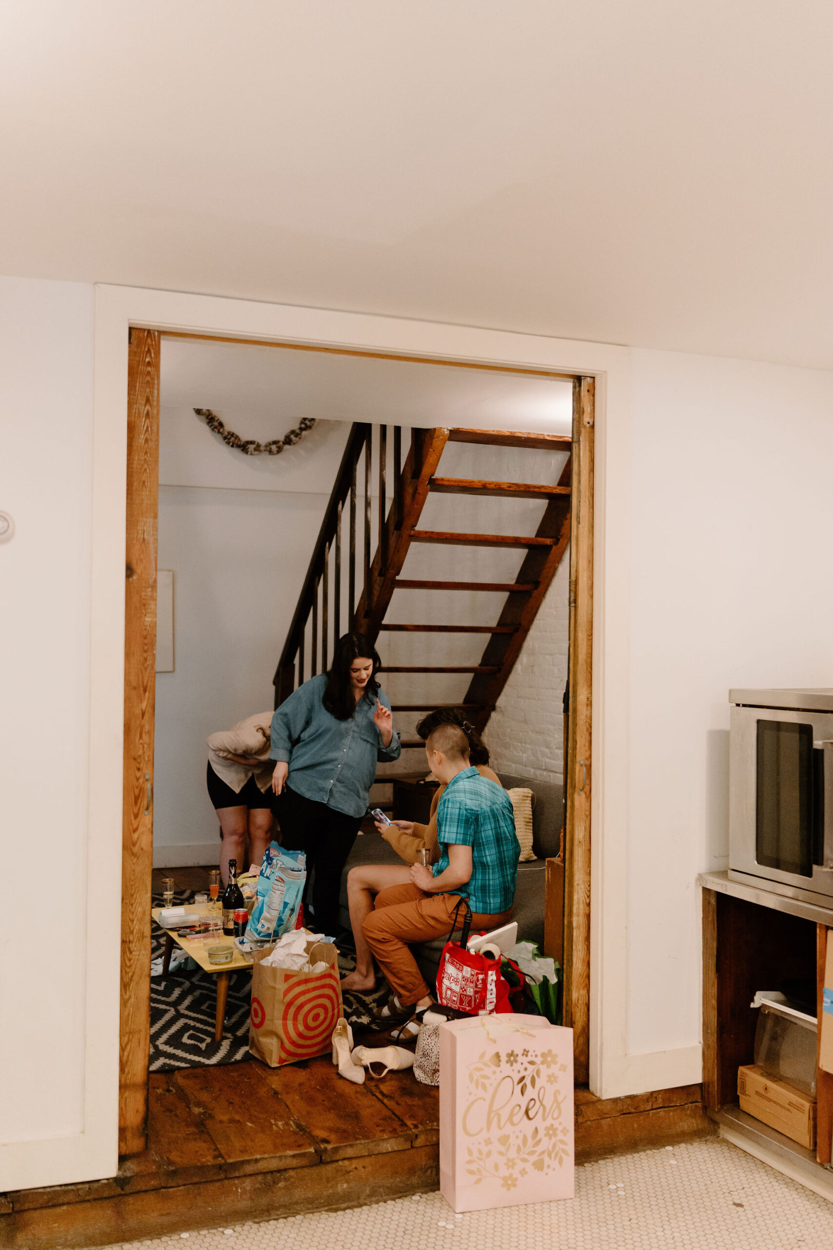 a group of friends sitting on a couch in a cluttered room, filled with bags and boxes, as they prepare for a wedding