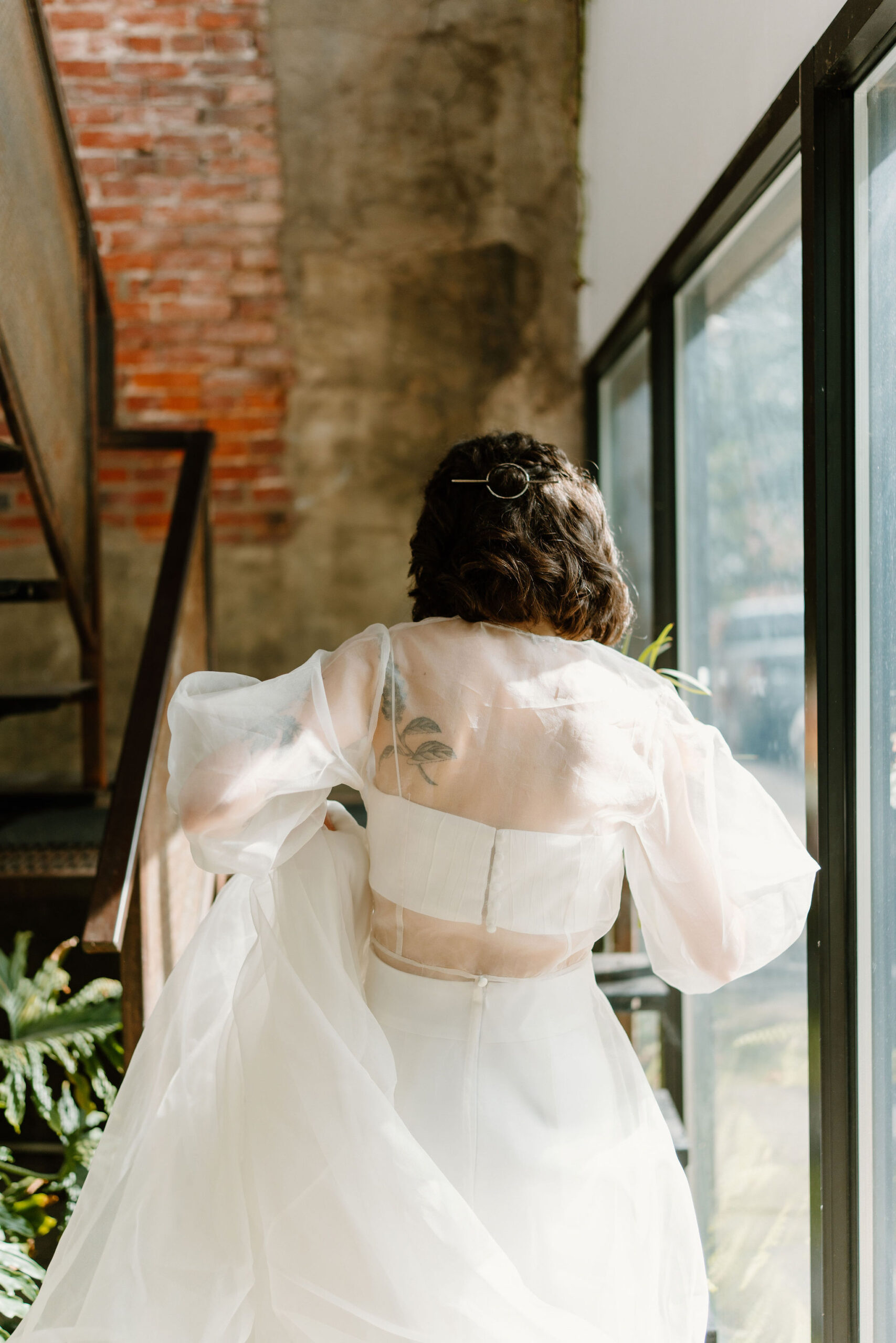 Bride walking away from the camera, holding up her skirt as she climbs an industrial staircase