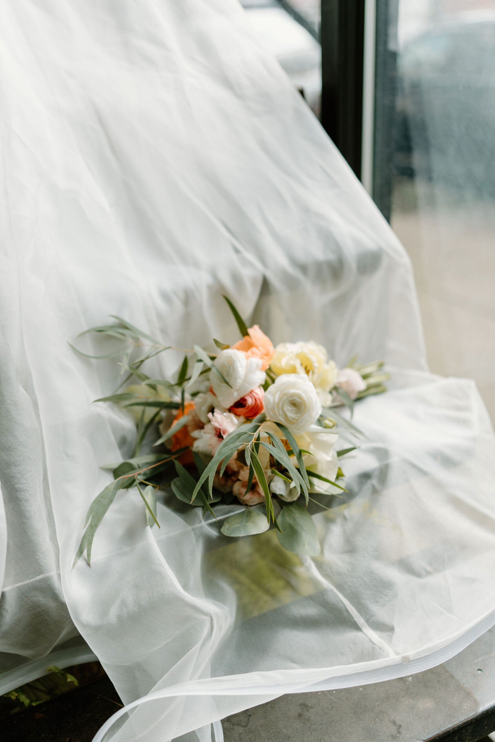 bridal bouquet of ranunculus, poppies, and greenery on a staircase, on top of a bride's sheer white cape and train