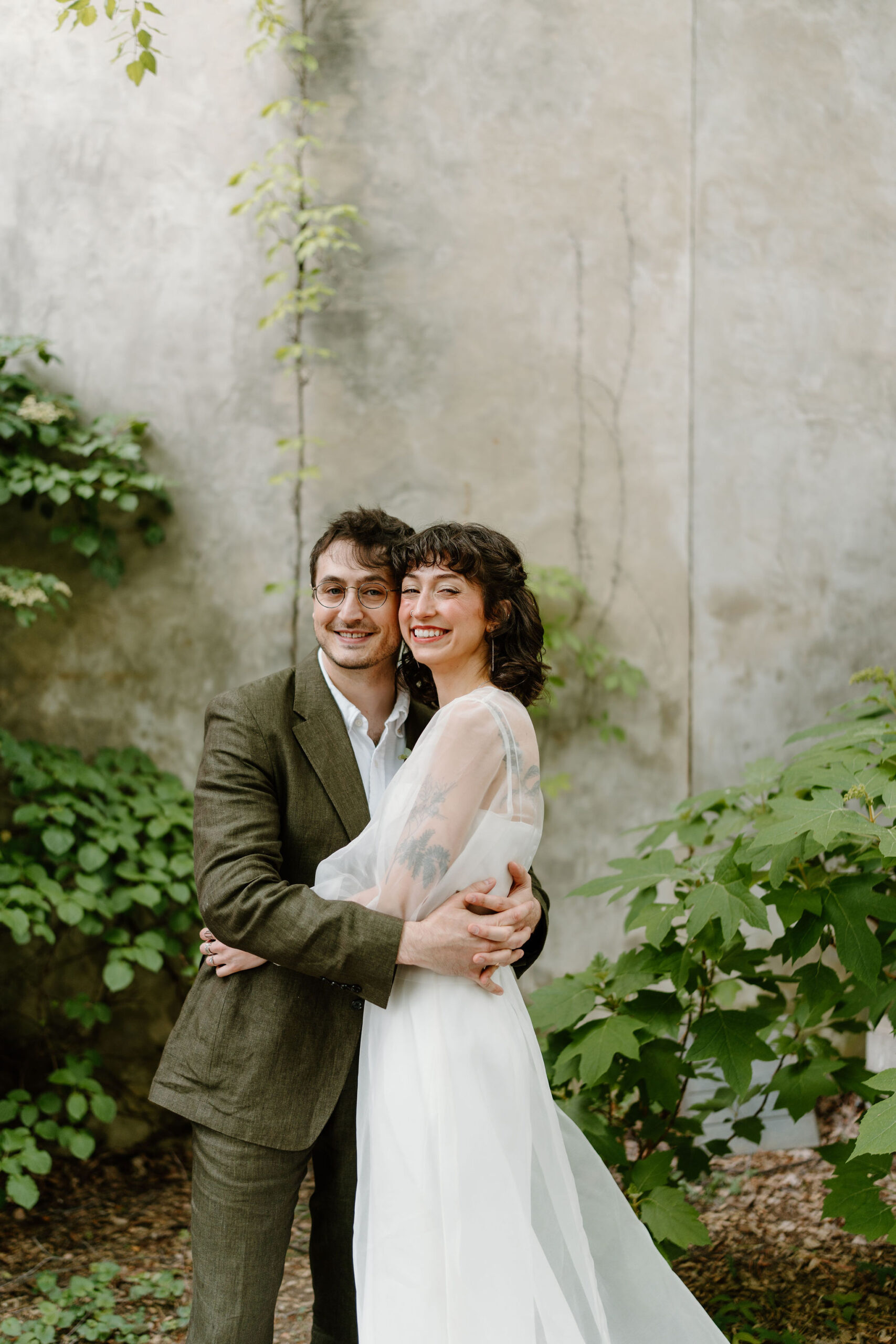 bride and groom embracing and smiling at the camera in a lush green cobblestone courtyard