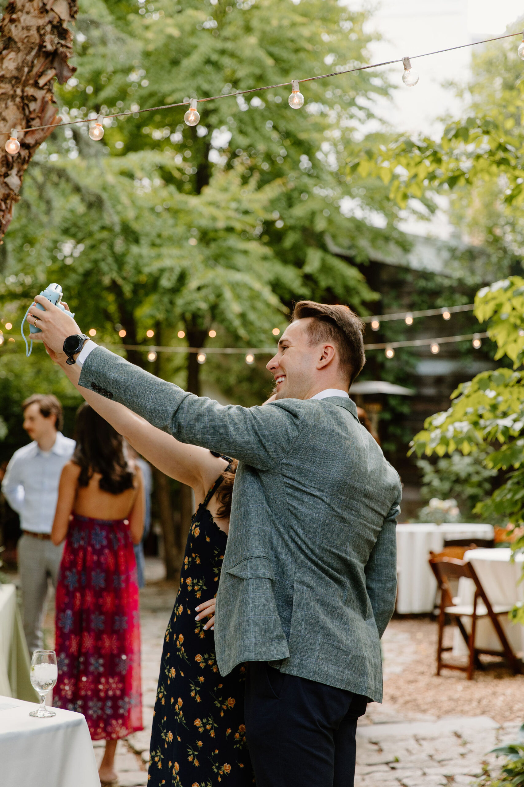 two guests taking a polaroid selfie by the guest book in a green courtyard