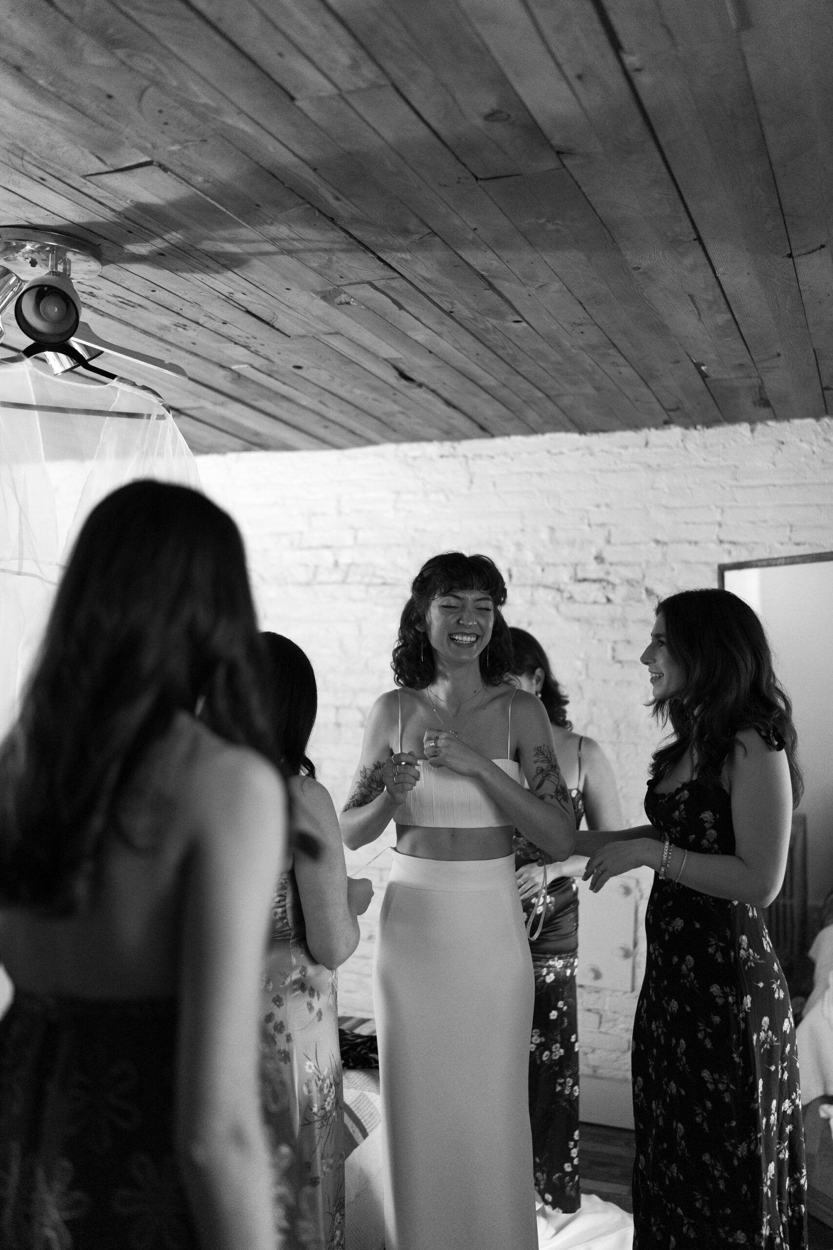 black and white image of a bride getting dressed with the help of her four friends, smiling as they surround her