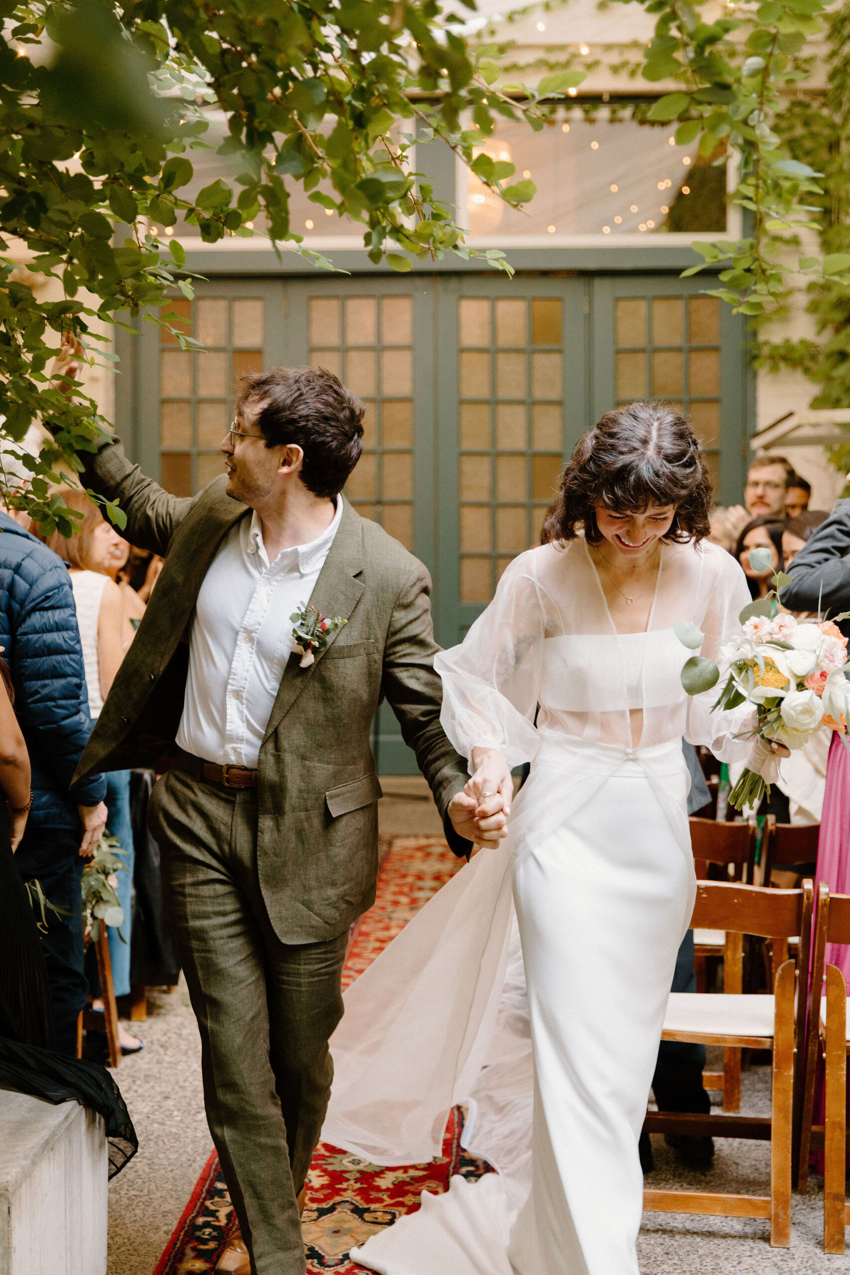 bride and groom holding hands as they exit their ceremony, bride smiling down while groom high fives a guest