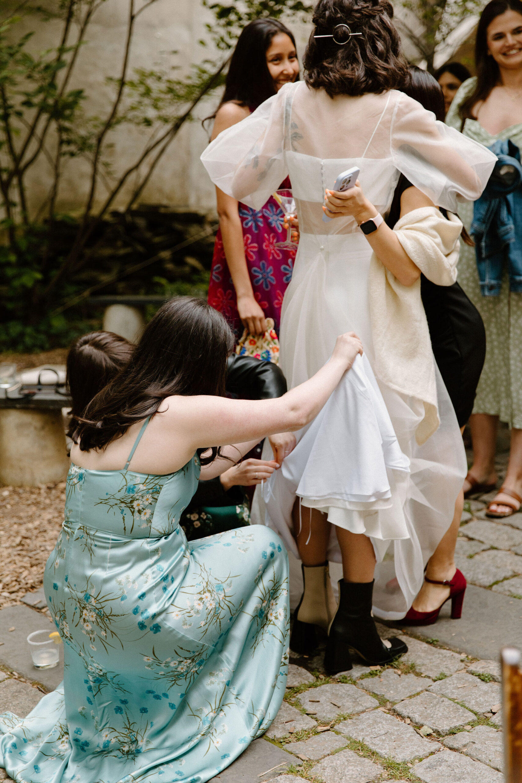 bride embracing guests, while her friends kneel behind her to bustle her train