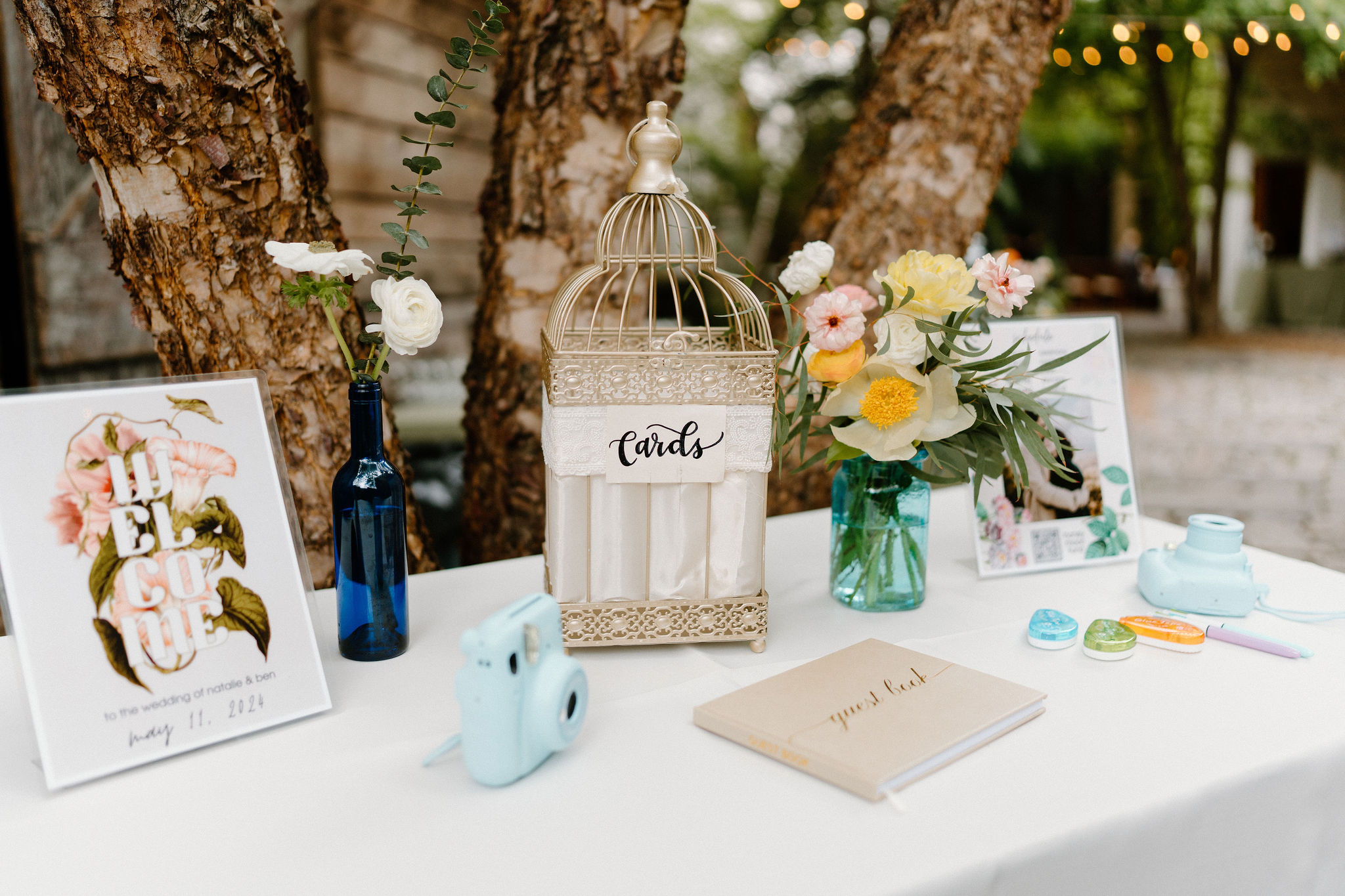 welcome table with a polaroid guest book, bird-cage card box, and schedule of events