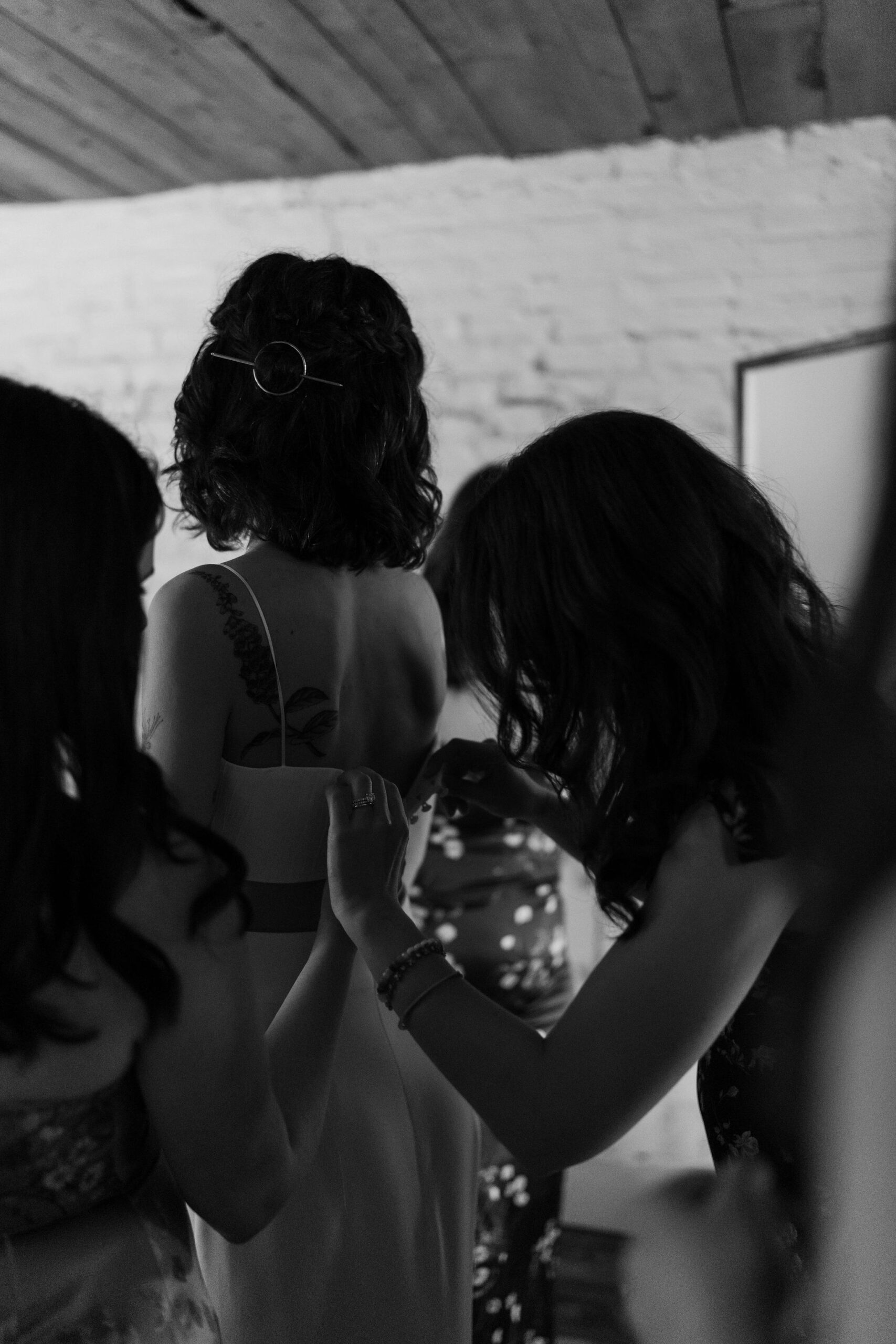 black and white image of a bride being buttoned into her two piece wedding dress by two of her friends