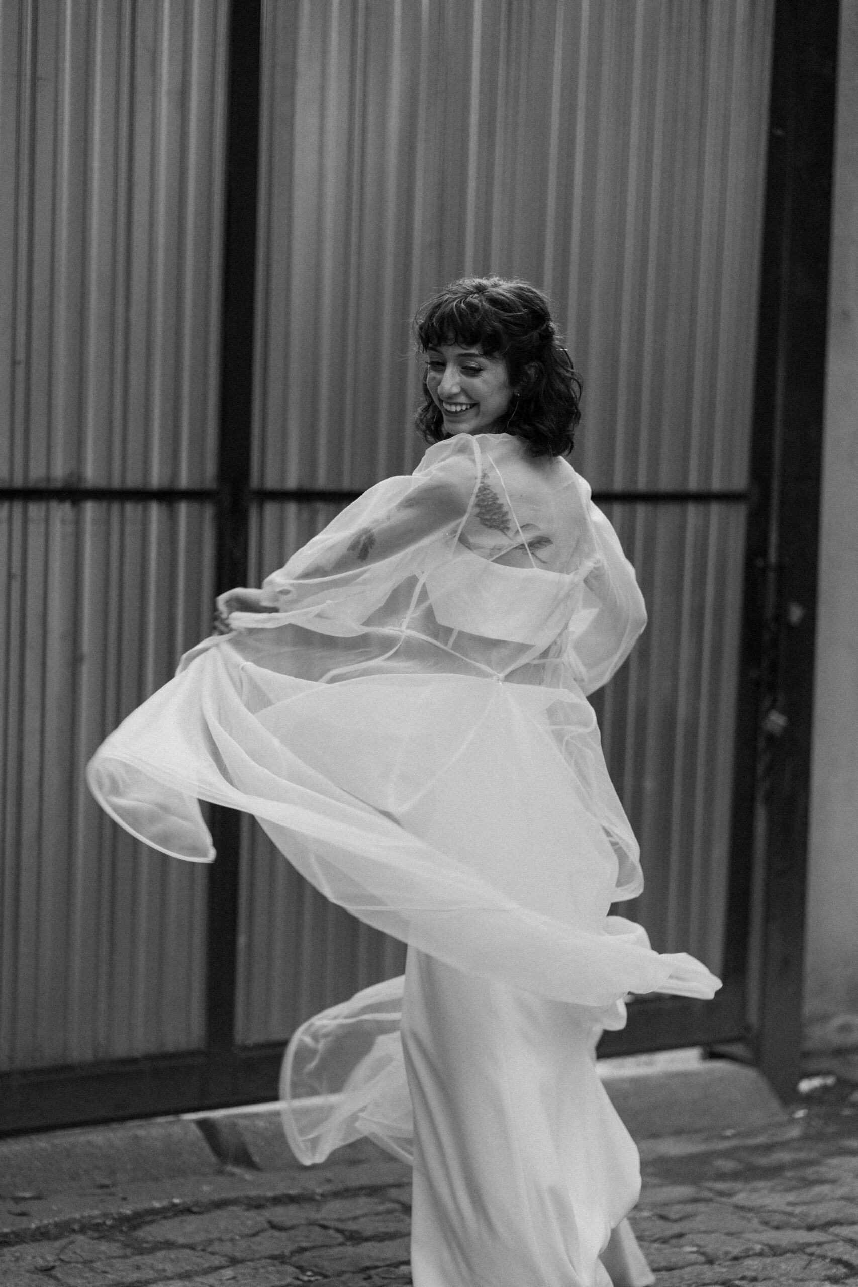 black and white, blurry image of a bride twirling her cape and smiling