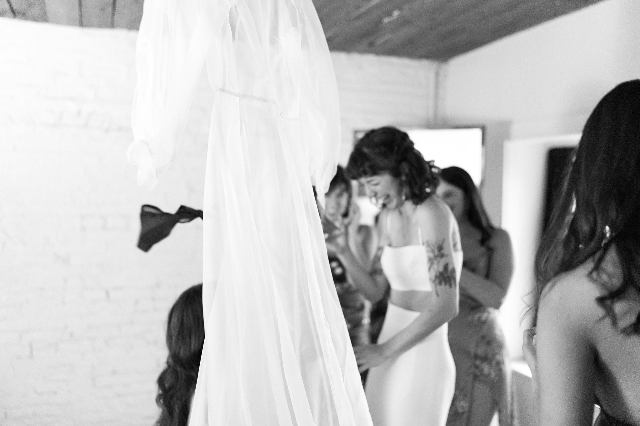 black and white image of a bride getting ready for her wedding day, surrounded by her friends, who are helping her change her undergarments