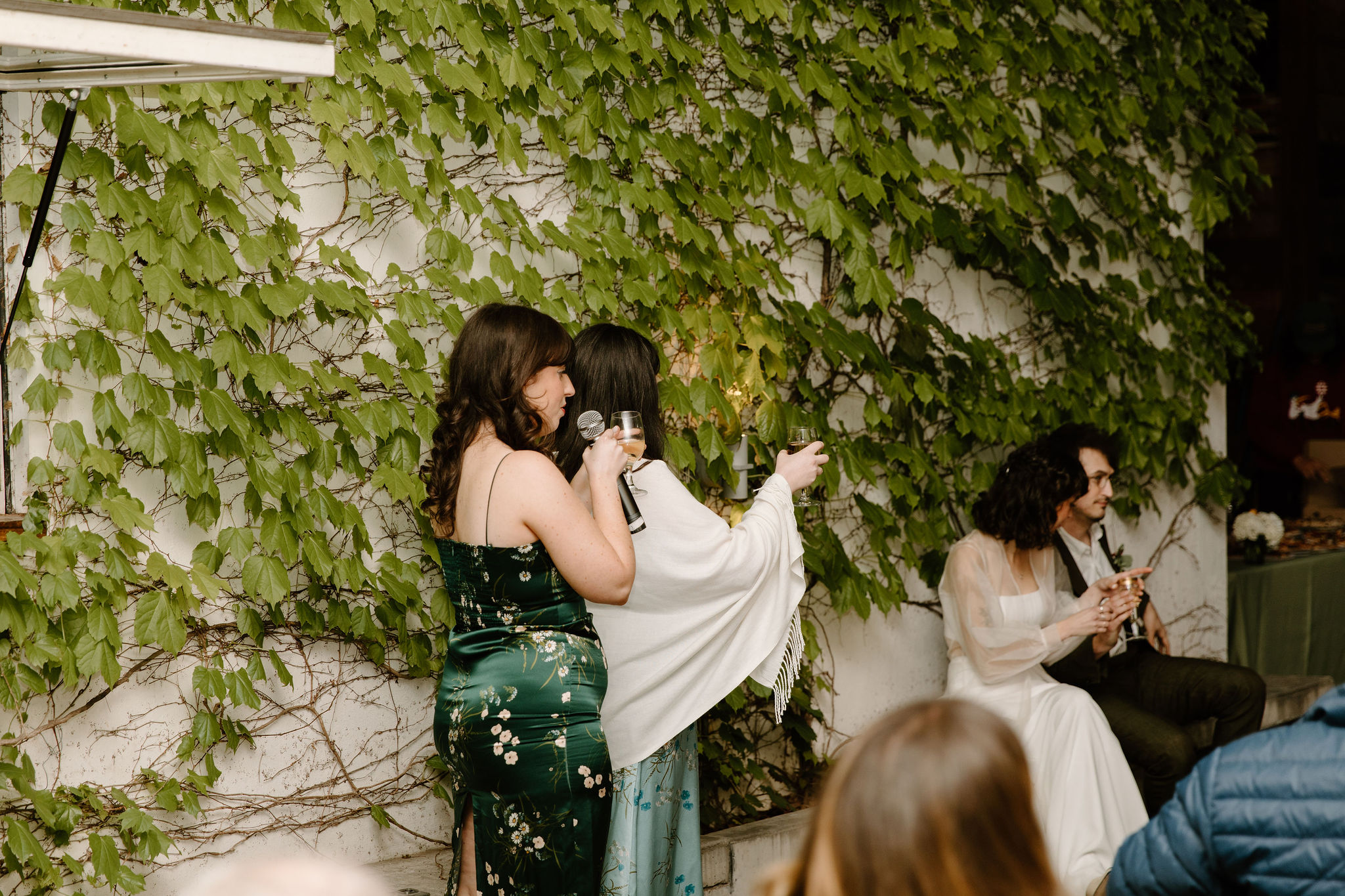 bride's two friends delivering a speech in front of an ivy wall