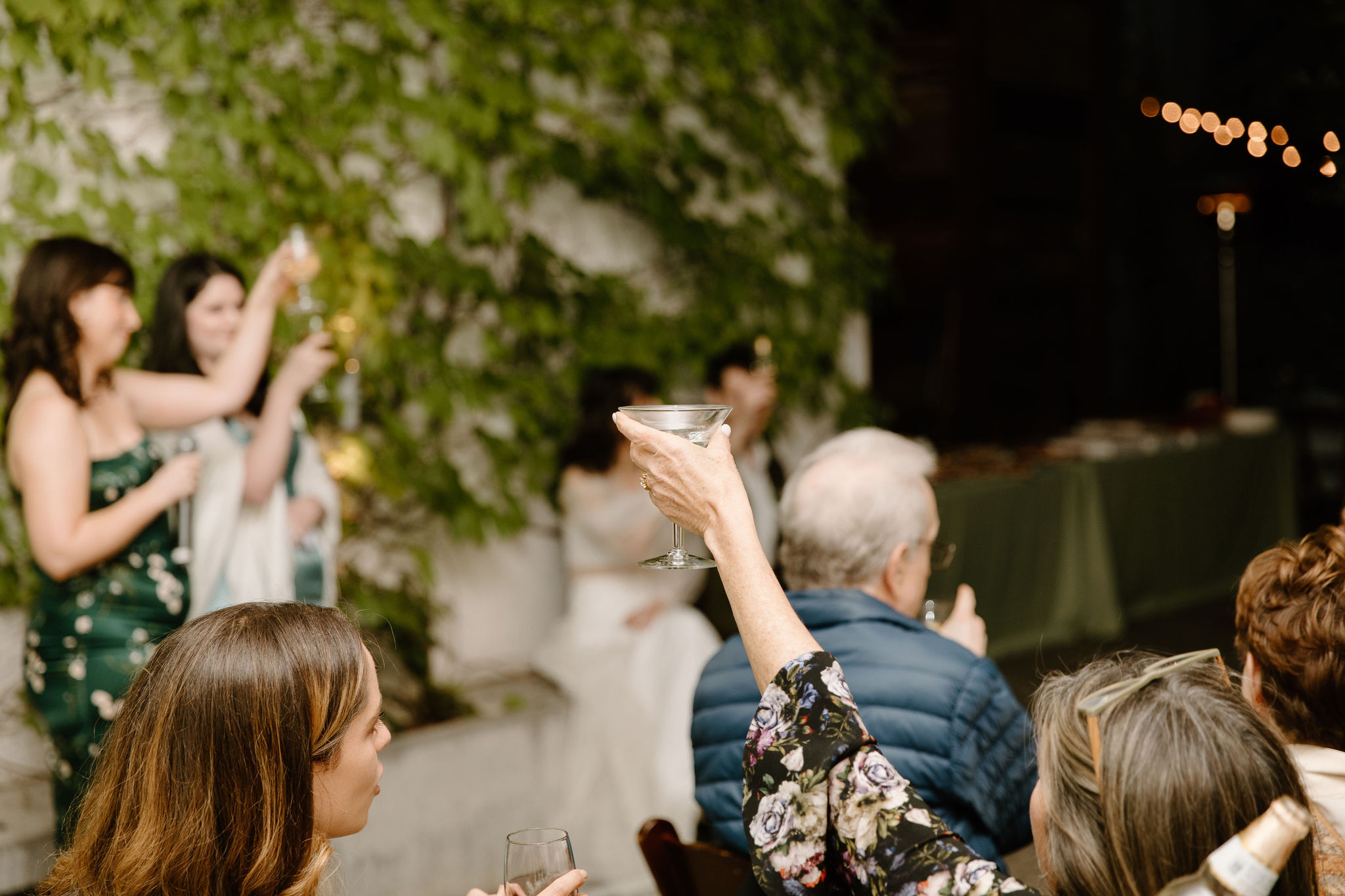 mother of the groom raising her martini class to cheers, while bride and groom sit in the background