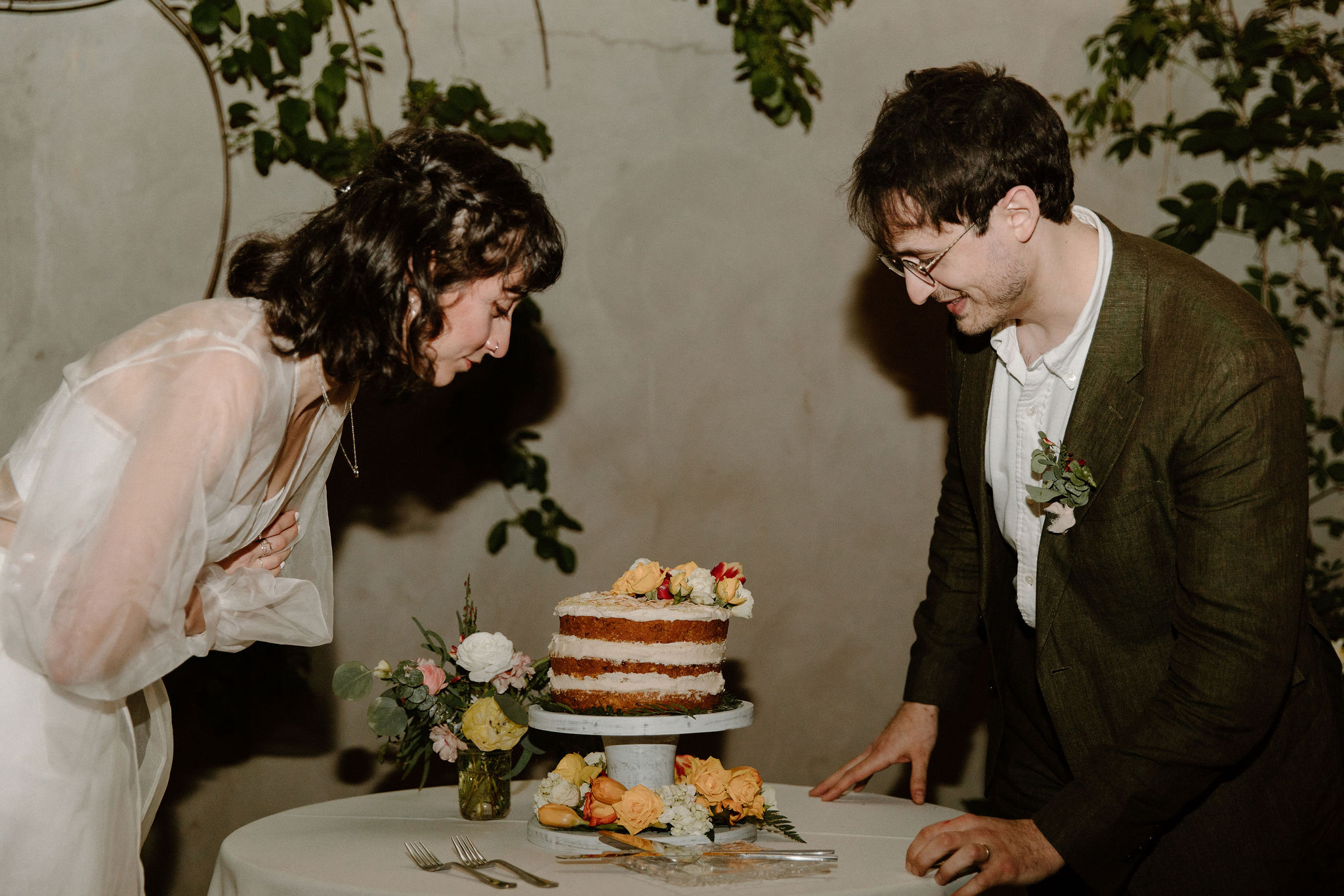 bride and groom on opposite sides of their wedding cake, admiring it