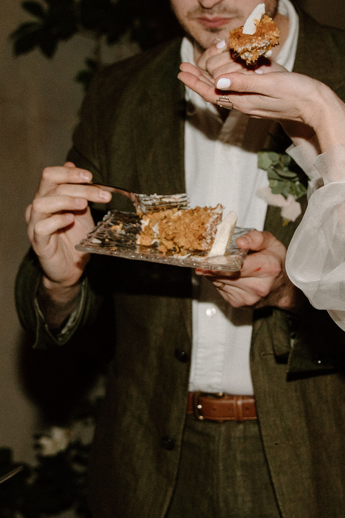 a close up of a bride and groom's hands as they each take a bit of their wedding cake