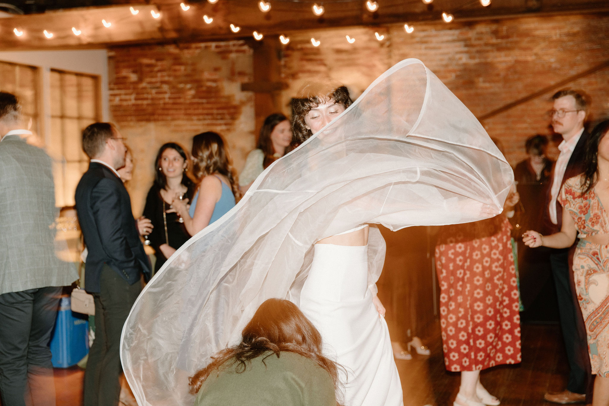 bride twirling the train of her sheer cape over her friend's head on the dance floor