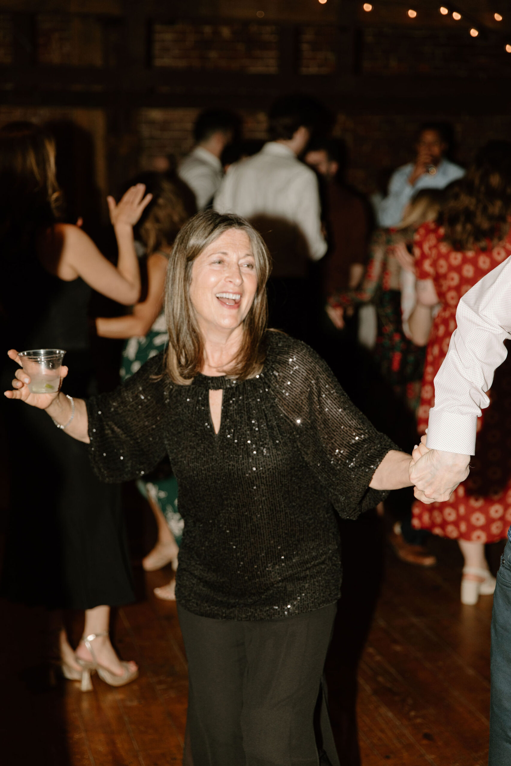 a guest smiling, holding her martini glass, and dancing during the wedding reception