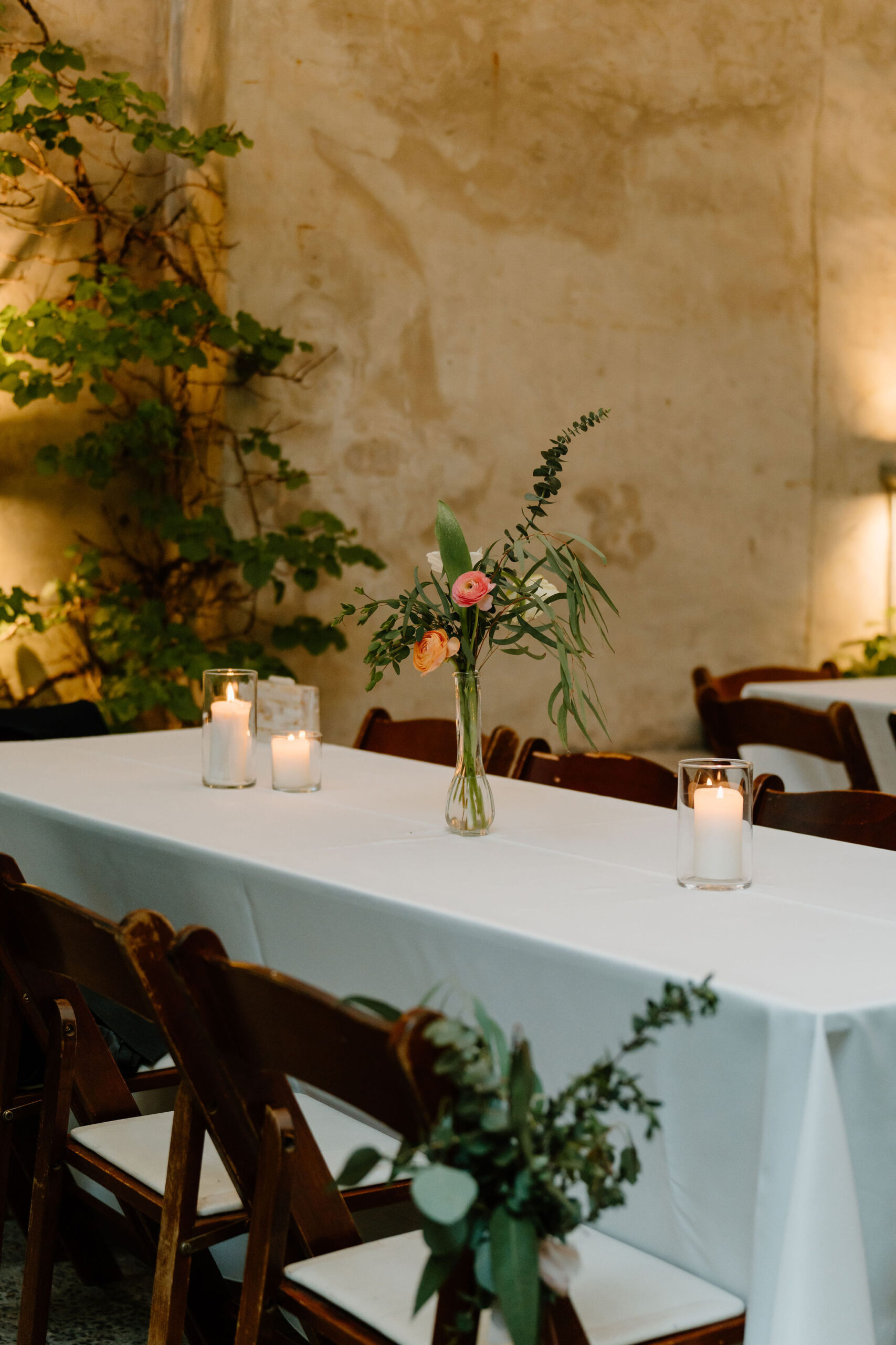 floral centerpieces in a thin tall vase, on a white tablecloth in a room filled with ivy