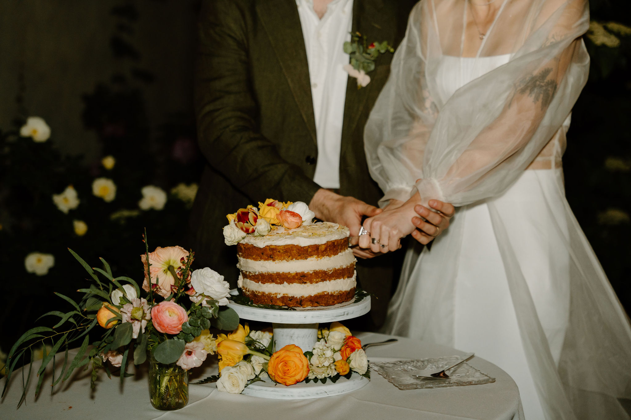 close up of a bride (wearing many rings) and groom's hands, cutting their wedding cake