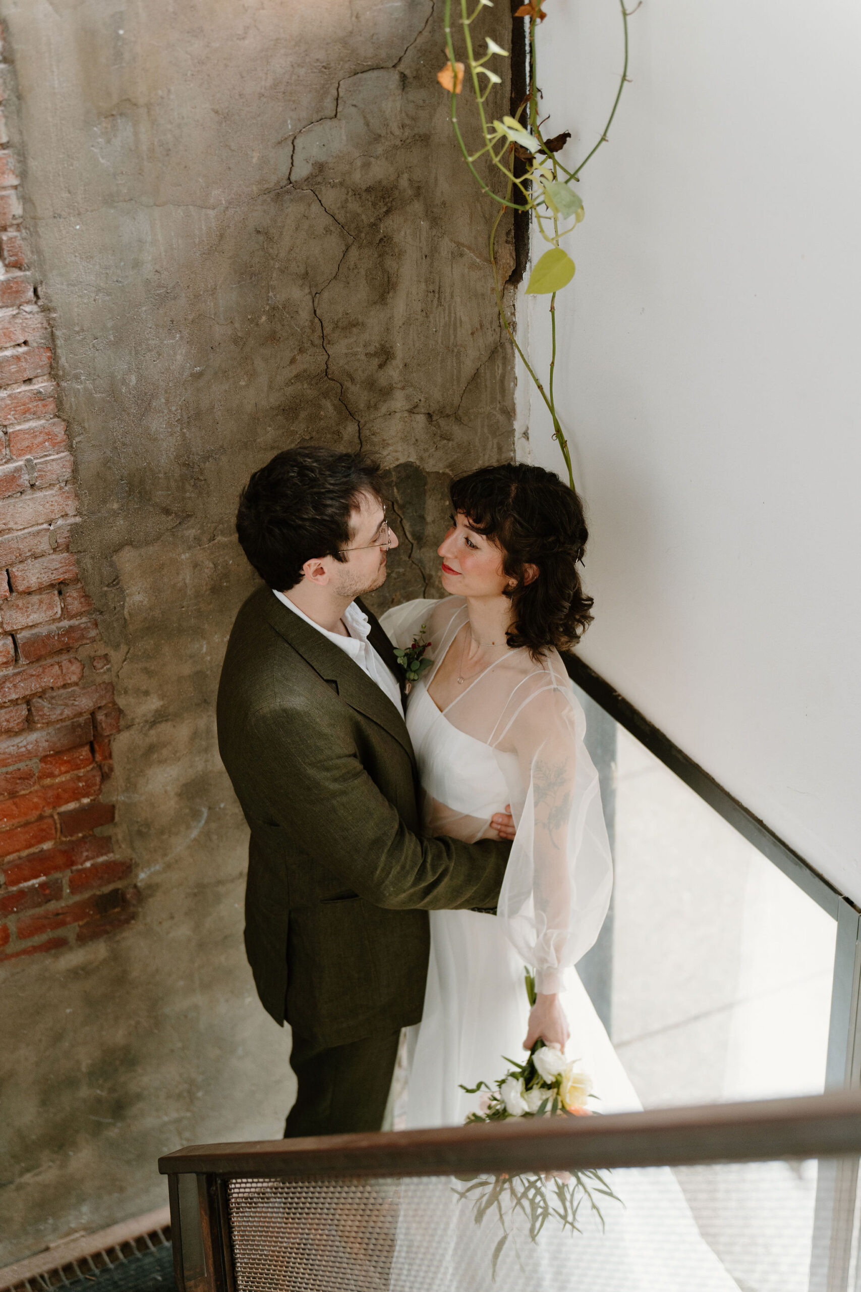 looking down on a bride and groom in an industrial stairwell as they embrace, smiling at each other