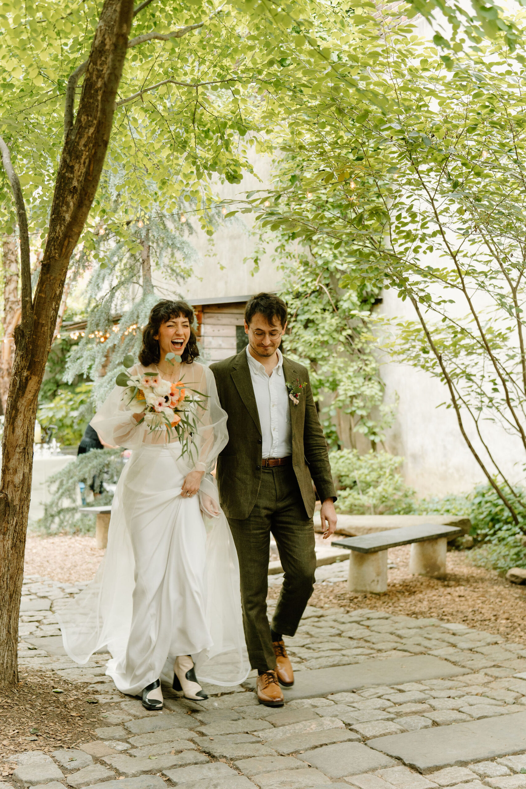 bride and groom entering their ceremony together, through a lush green courtyard