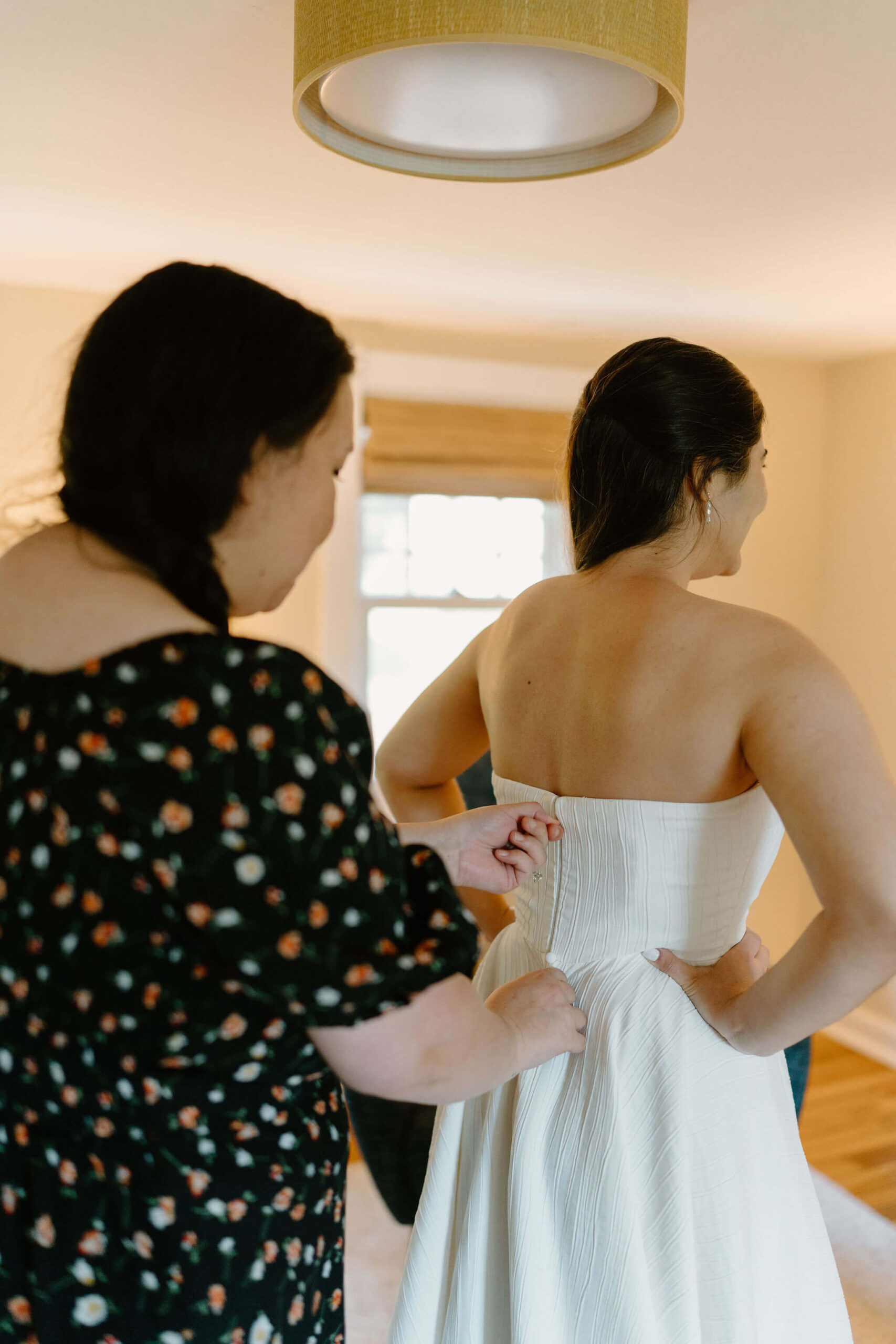 bride's friend (black floral dress) zipping up the bride's strapless wedding gown