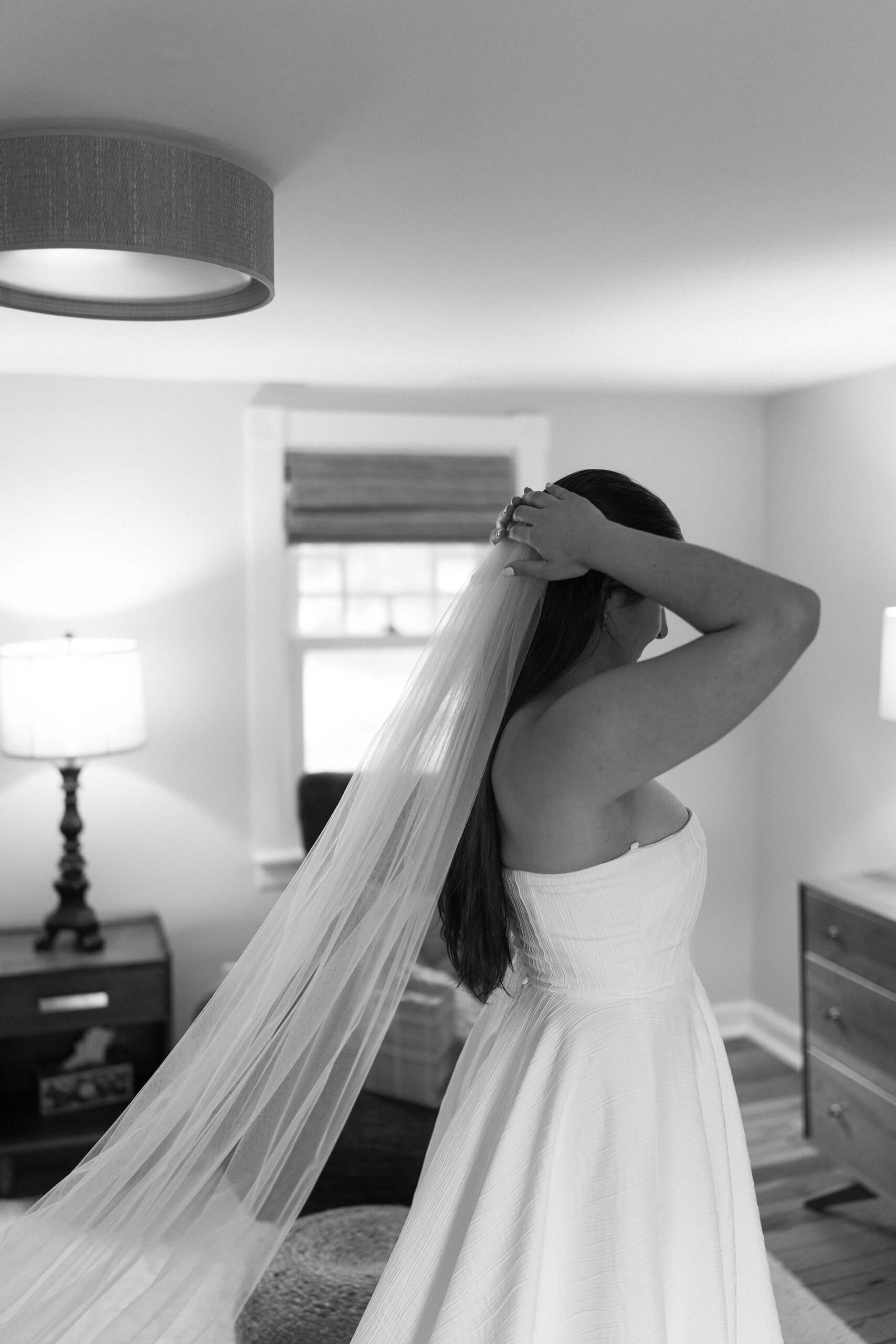 black and white image of bride pressing veil into her long brown hair, wearing strapless wedding gown