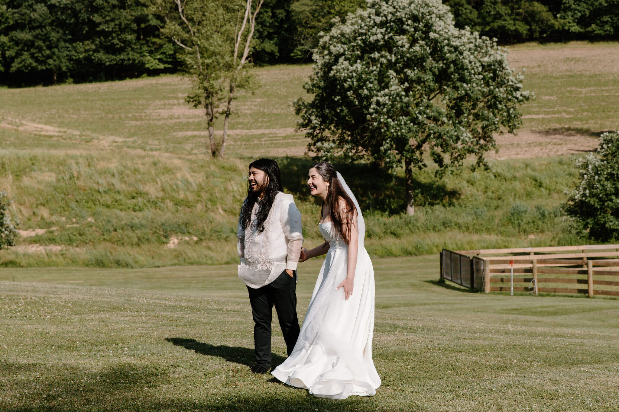 bride and groom holding hands and laughing toward their guests during their wedding ceremony, standing in a grassy field