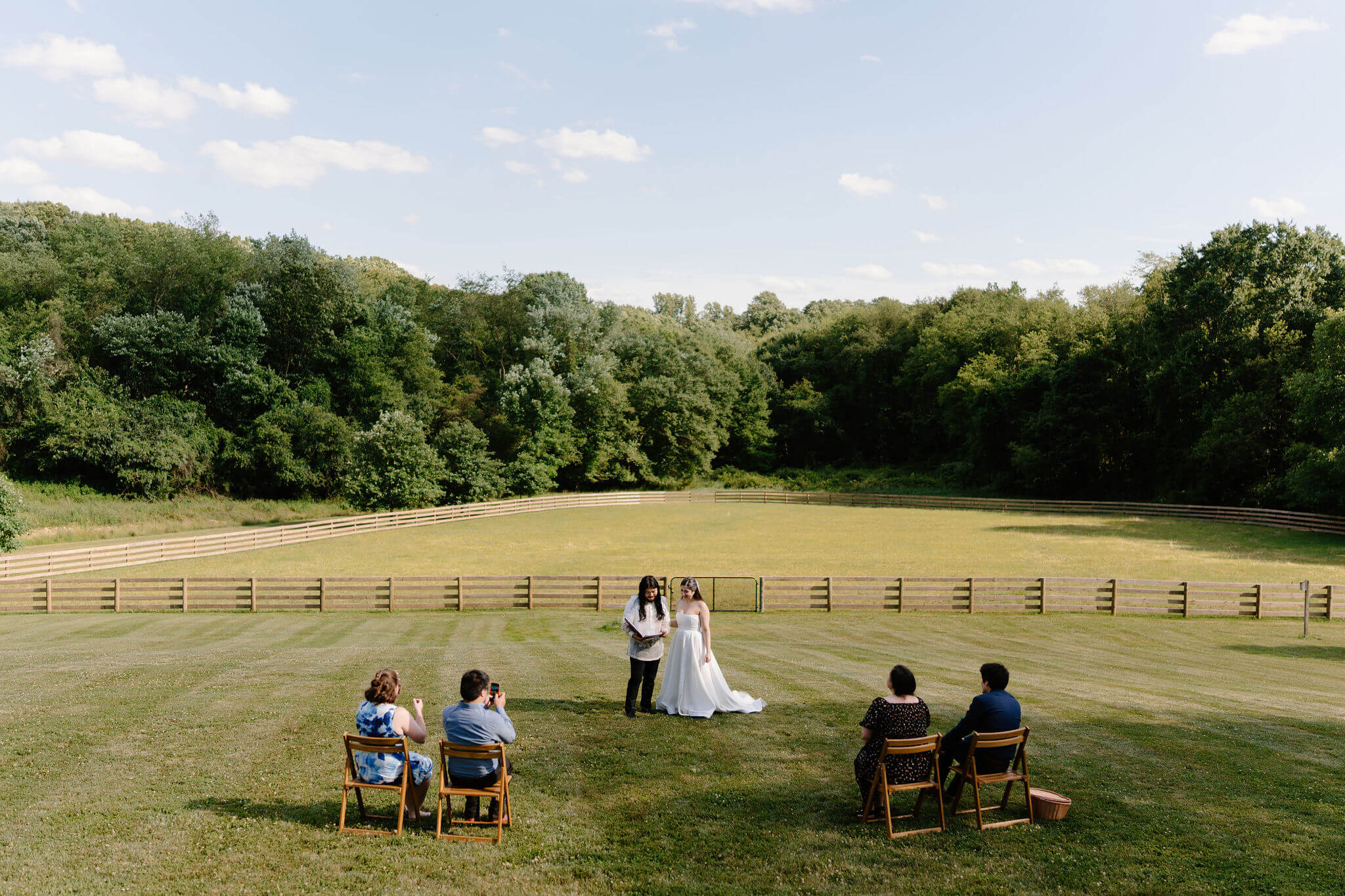 bride and groom standing in their self uniting ceremony, reading out of a binder to the four friends witnessing their marriage, in an open field on a sunny day