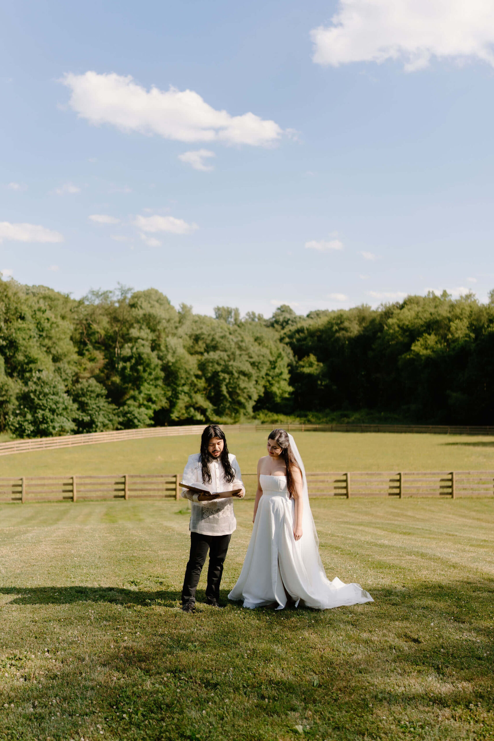 bride and groom standing in their self uniting wedding ceremony, reading out of a binder in an open field on a sunny day