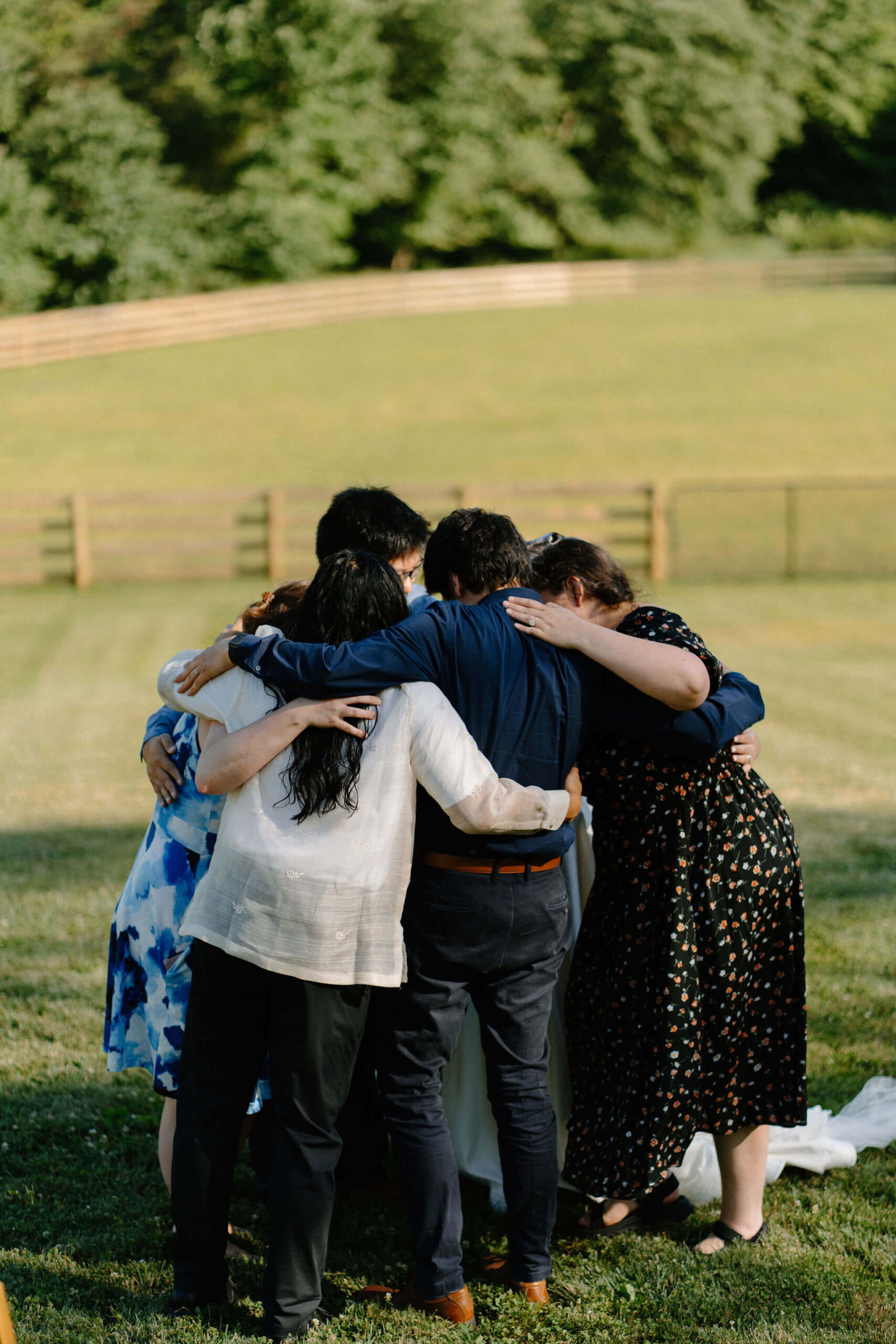 bride, groom, and four of their friends celebrating their marriage with a group hug in a grassy field