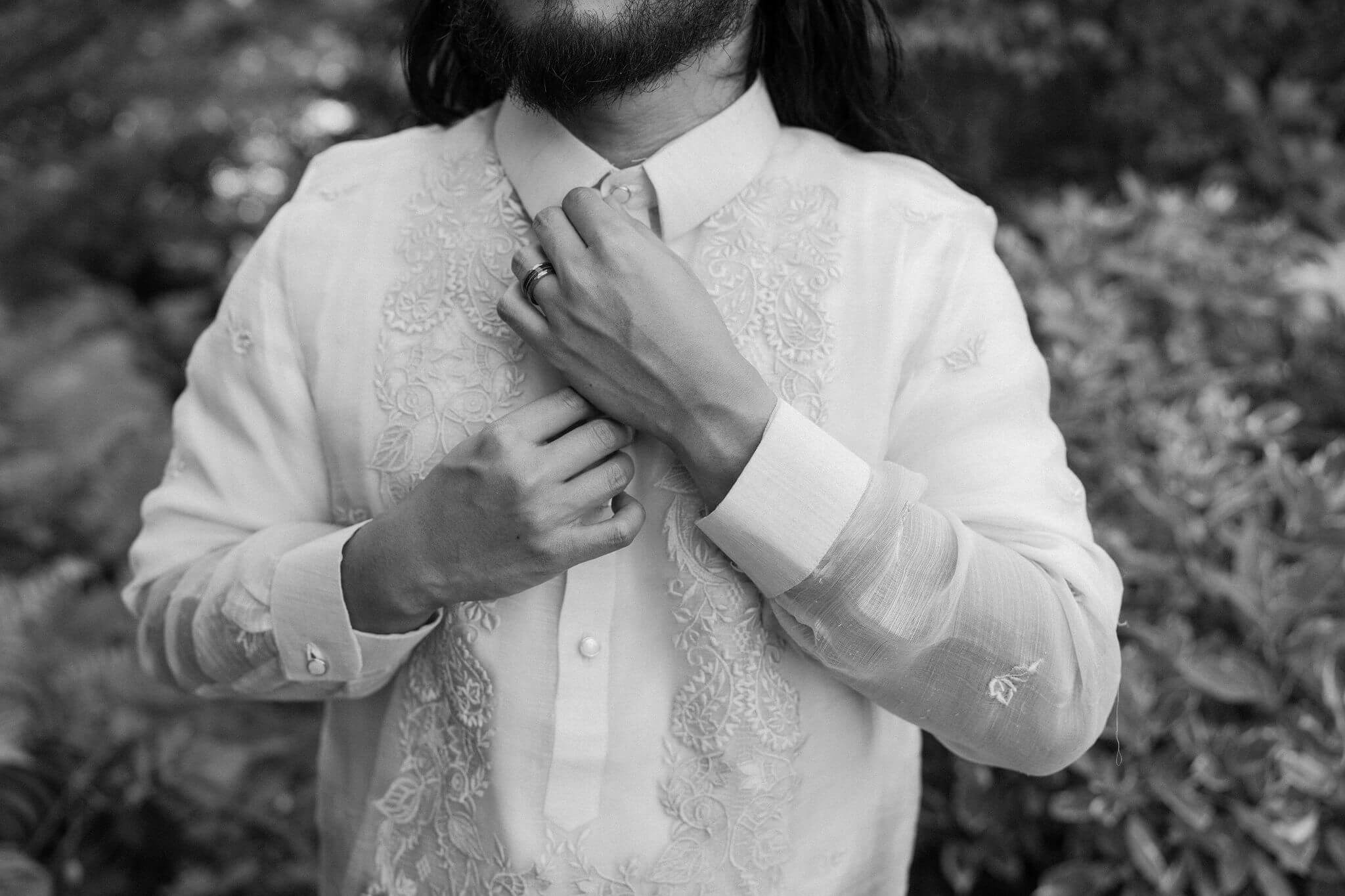 close-up black and white image of groom's hands straightening the collar on his shirt, focusing on his wedding band