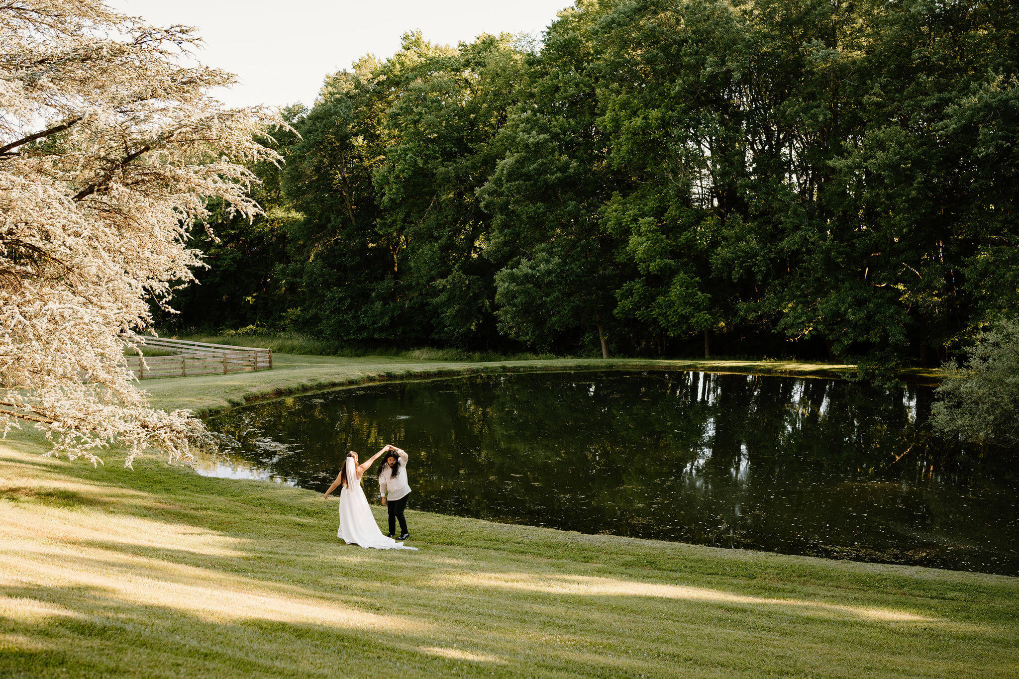 bride and groom holding hands and walking through a field away from the camera toward a pond, while groom is twirled in a spin