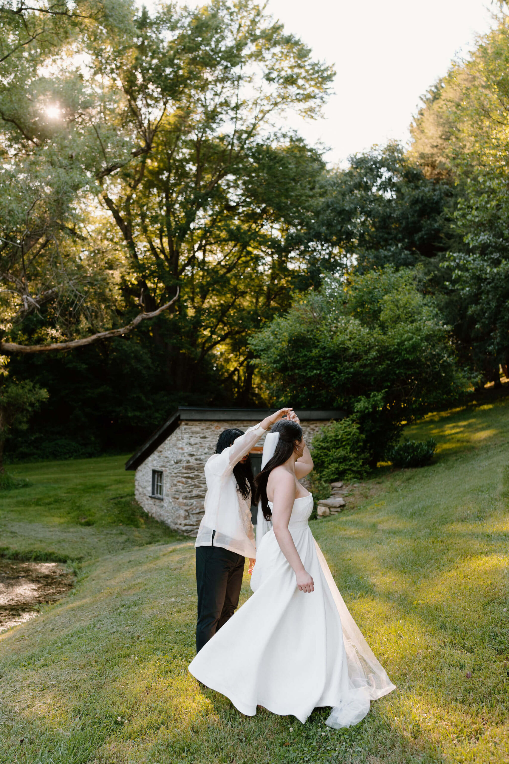 bride and groom next to a pond, surrounded by tall green trees, dancing and smiling at each other