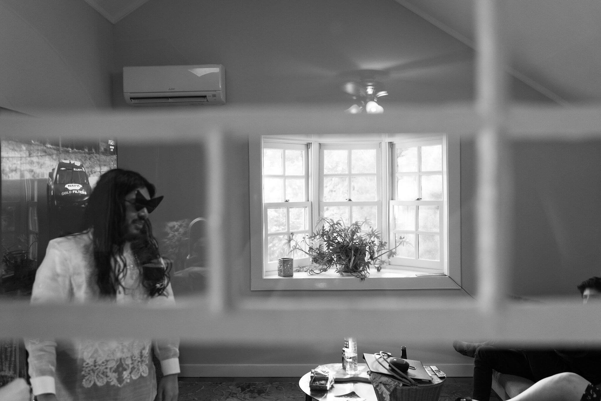 black and white image through a glass window of groom wearing silly large black sunglasses indoors