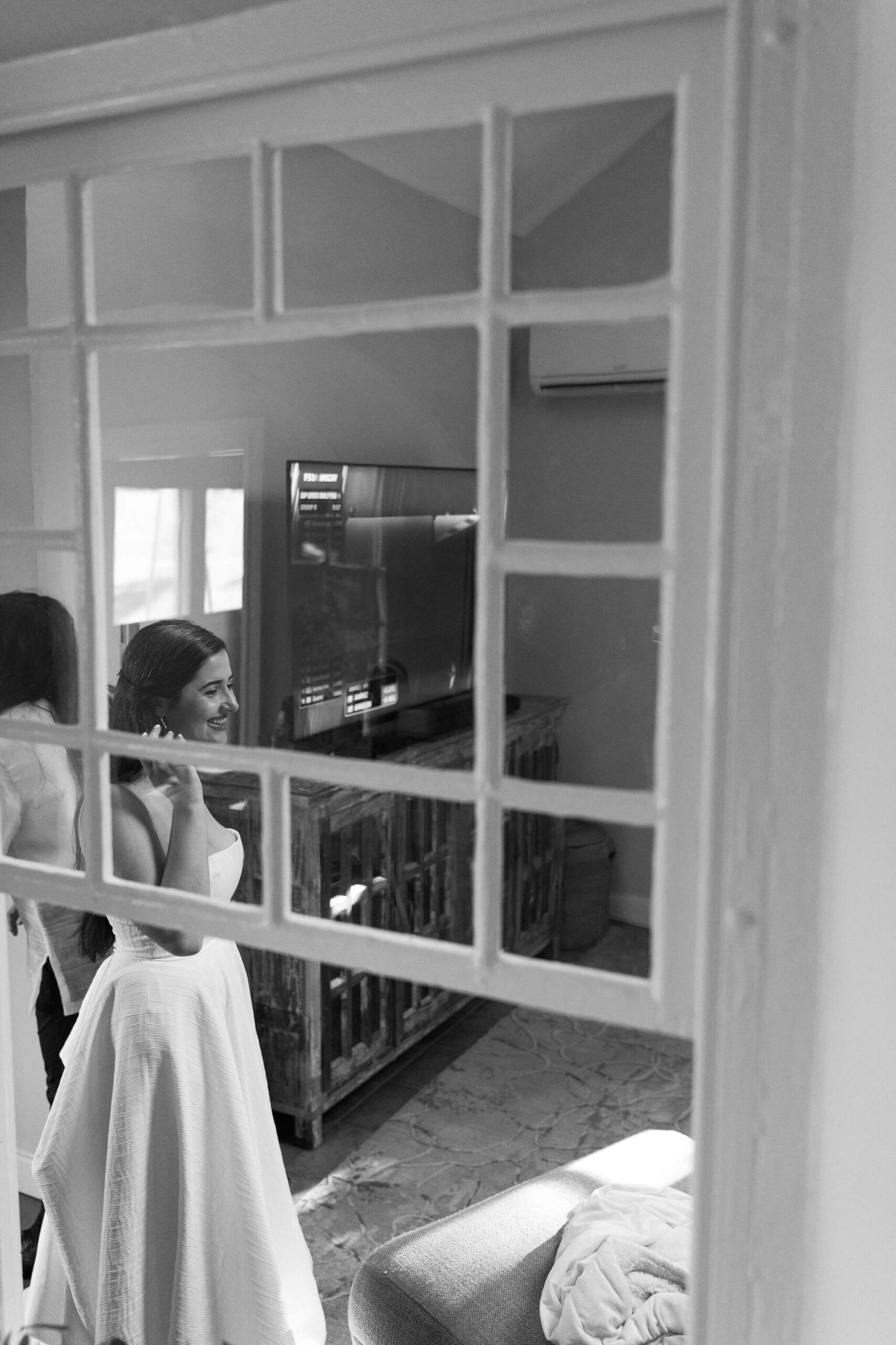 black and white image through a glass window of bride smiling toward her friends