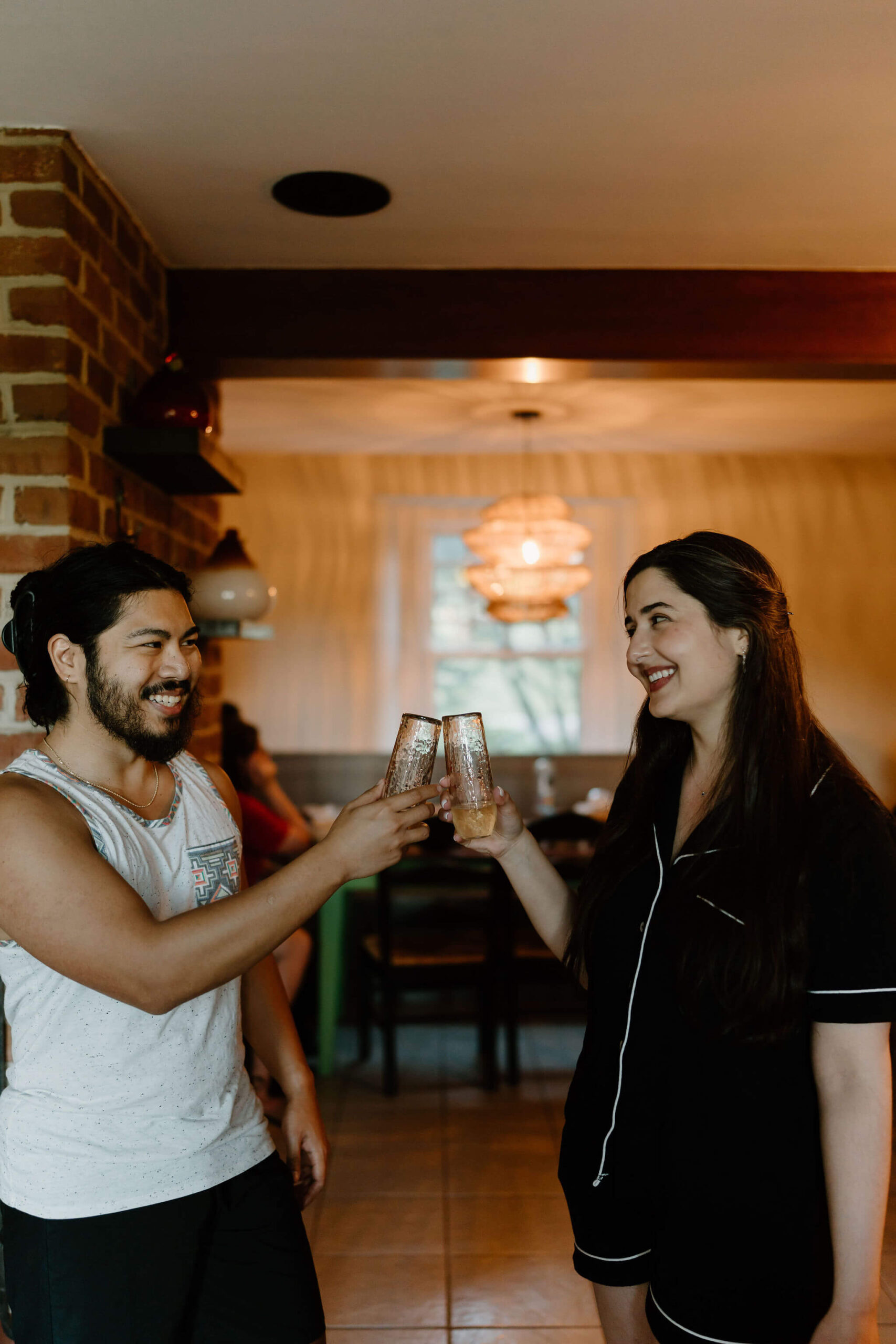 bride and groom, both in pajamas, having a toast with their champagne flutes and smiling at each other