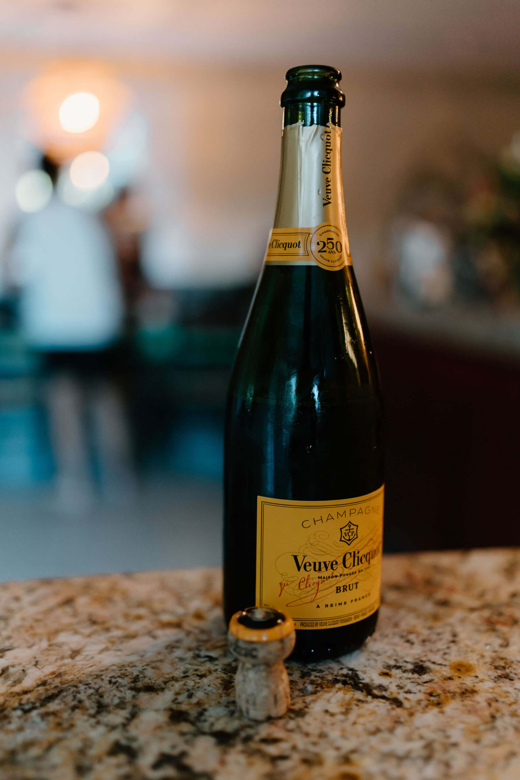 close up bottle of champagne on a kitchen counter, with a cork sitting in front of it