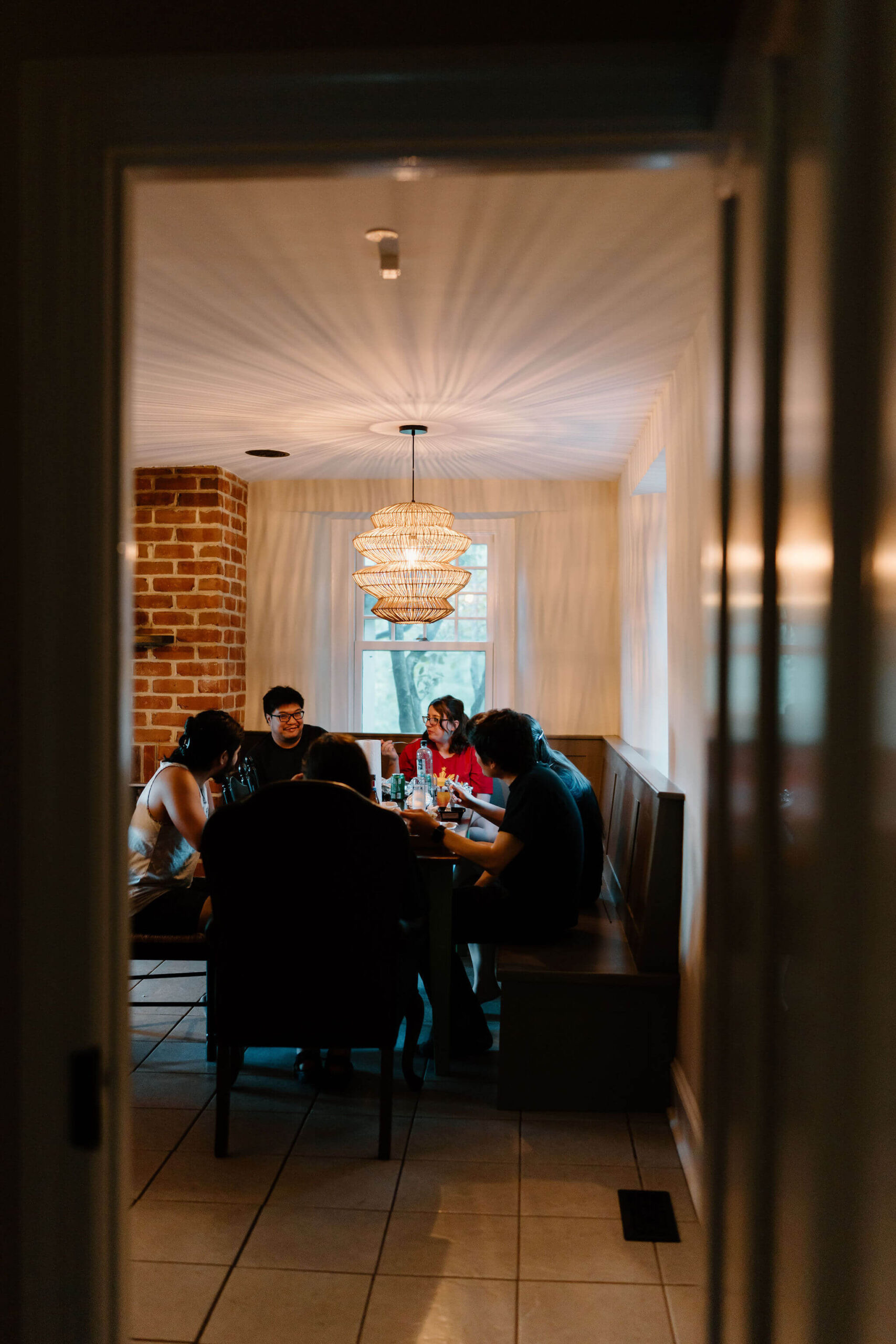 view through a doorframe of six friends sitting at a long wooden kitchen table, all wearing pajamas, eating dinner