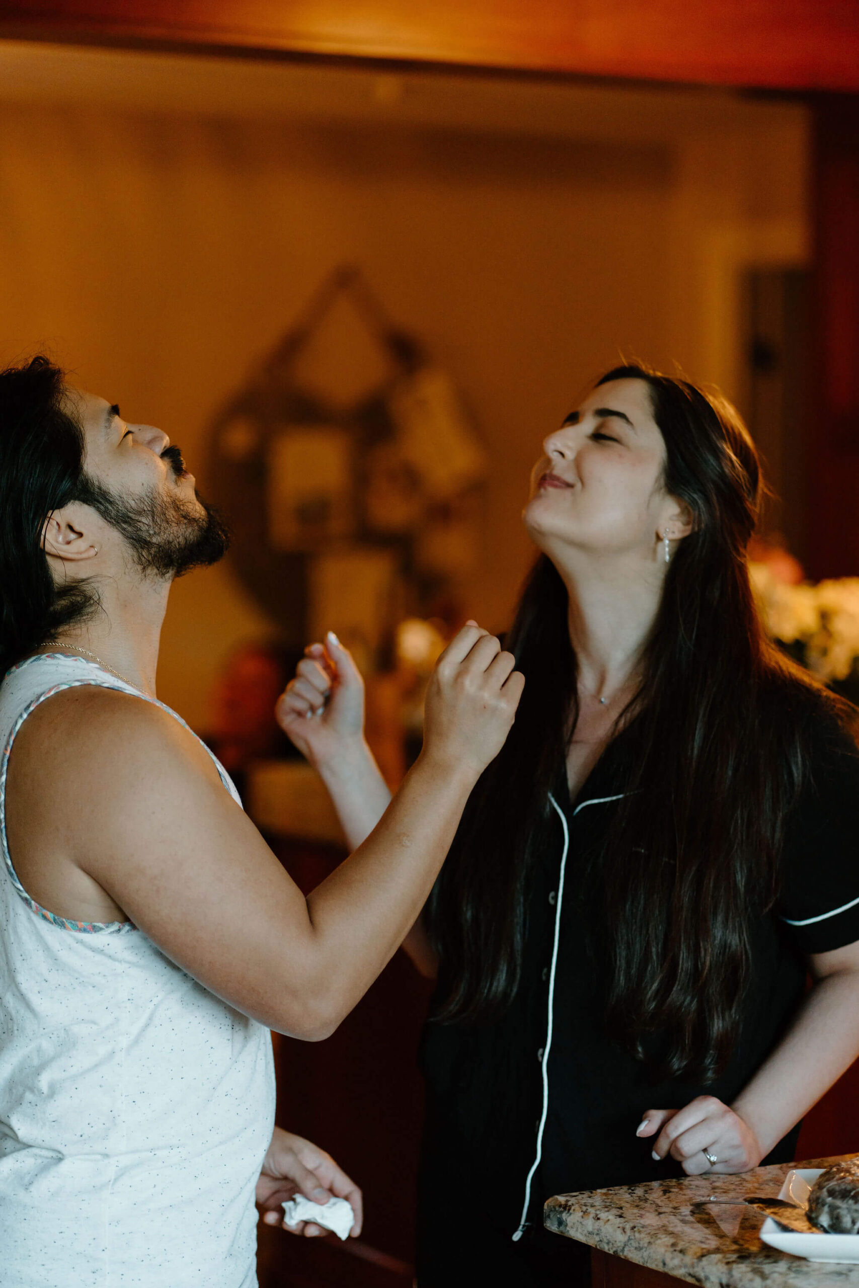 bride and groom (both in pajamas) feeding each other pieces of a large chocolate doughnut in lieu of a wedding cake