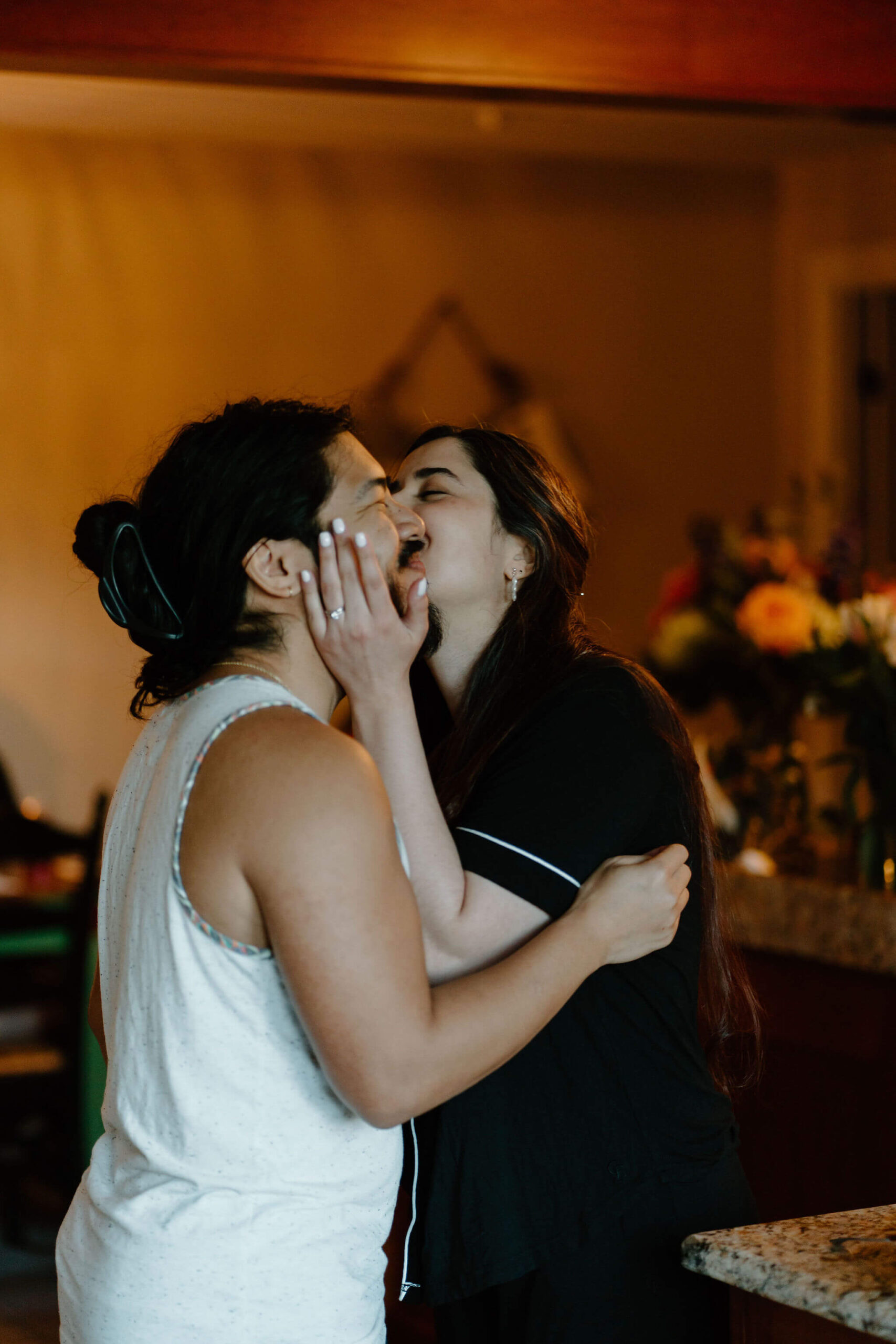 bride holding groom's face and kissing him on the cheek, both wearing pajamas and smiling