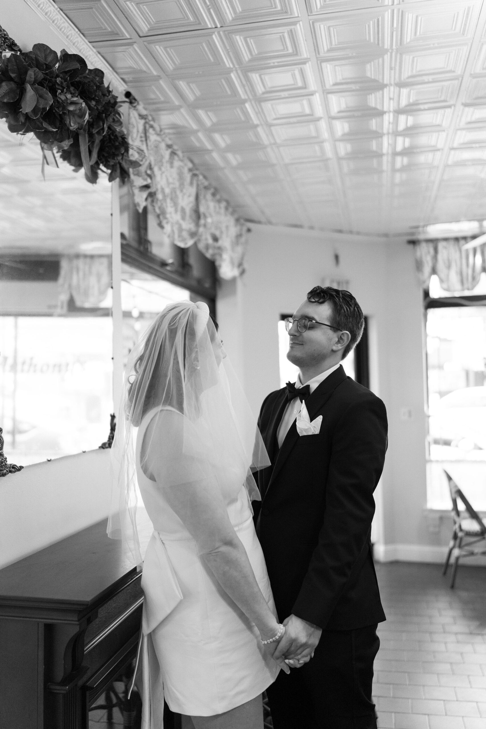 black and white image of bride and groom holding hands and smiling softly, facing each other, inside the coffee shop