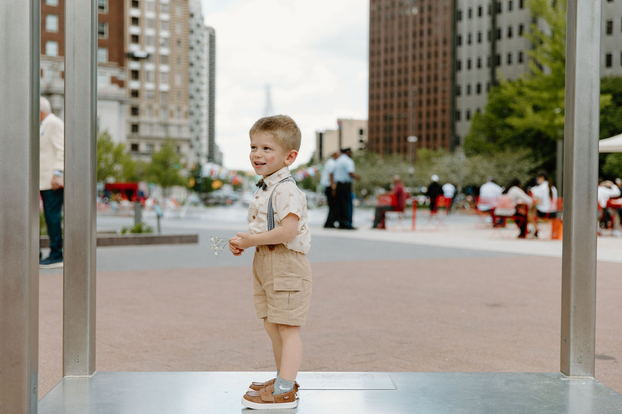 close up of bride's young nephew, wearing khaki shorts and overalls, smiling off camera